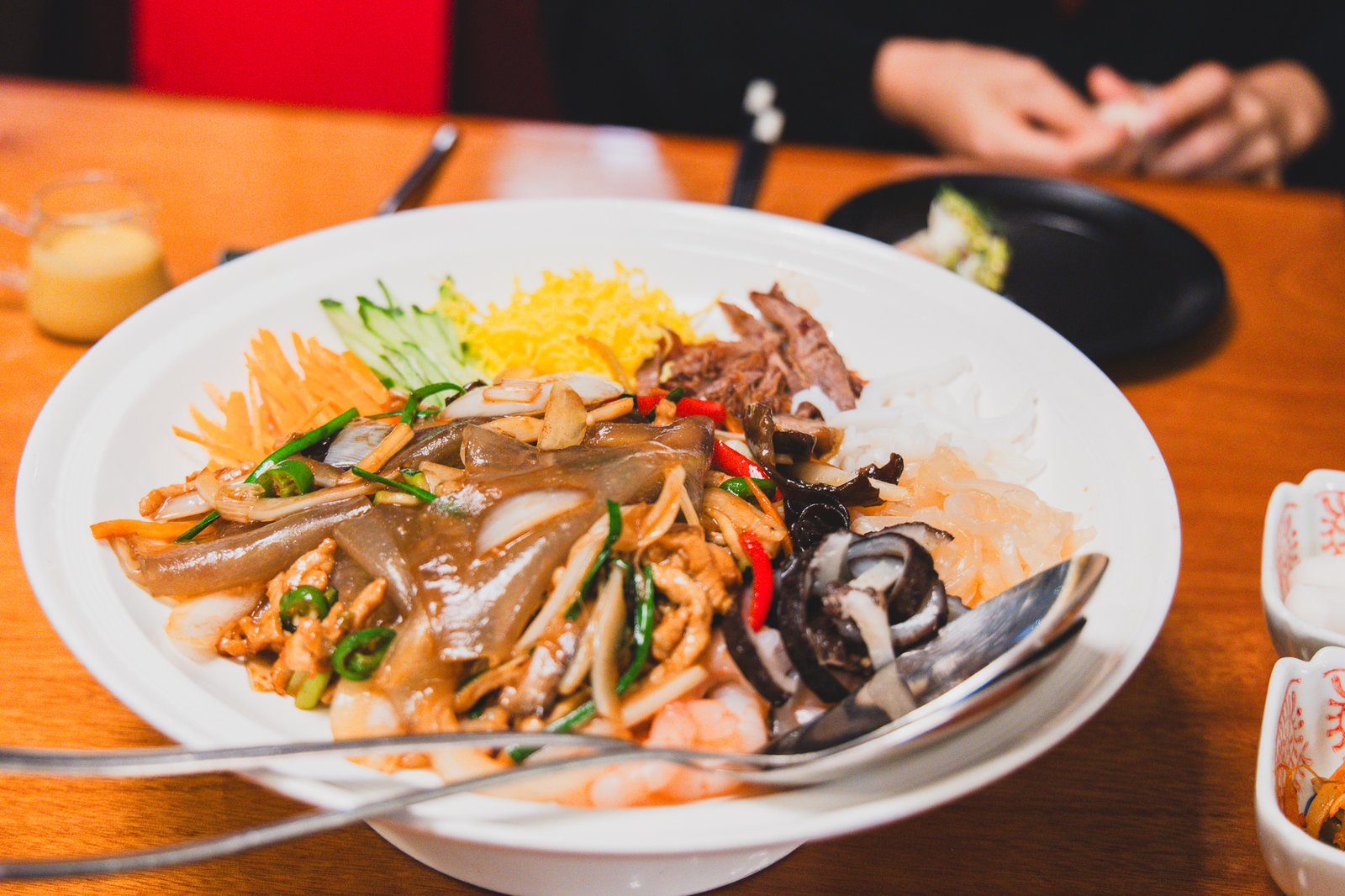 An overhead view of palsaek-yangjangpi, a platter with color-coded sections of carrot, cucumber, translucent starch sheets, black fungus, shredded duck, and shrimp arranged around the edge
