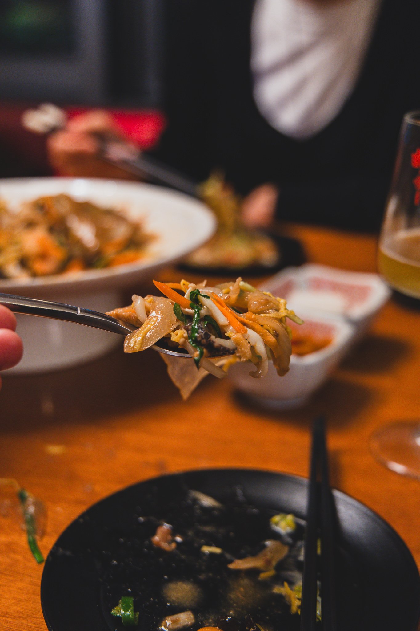 A close-up of chopsticks lifting a tangle of mixed yangjangpi ingredients, coated in mustard sauce, out of the serving platter