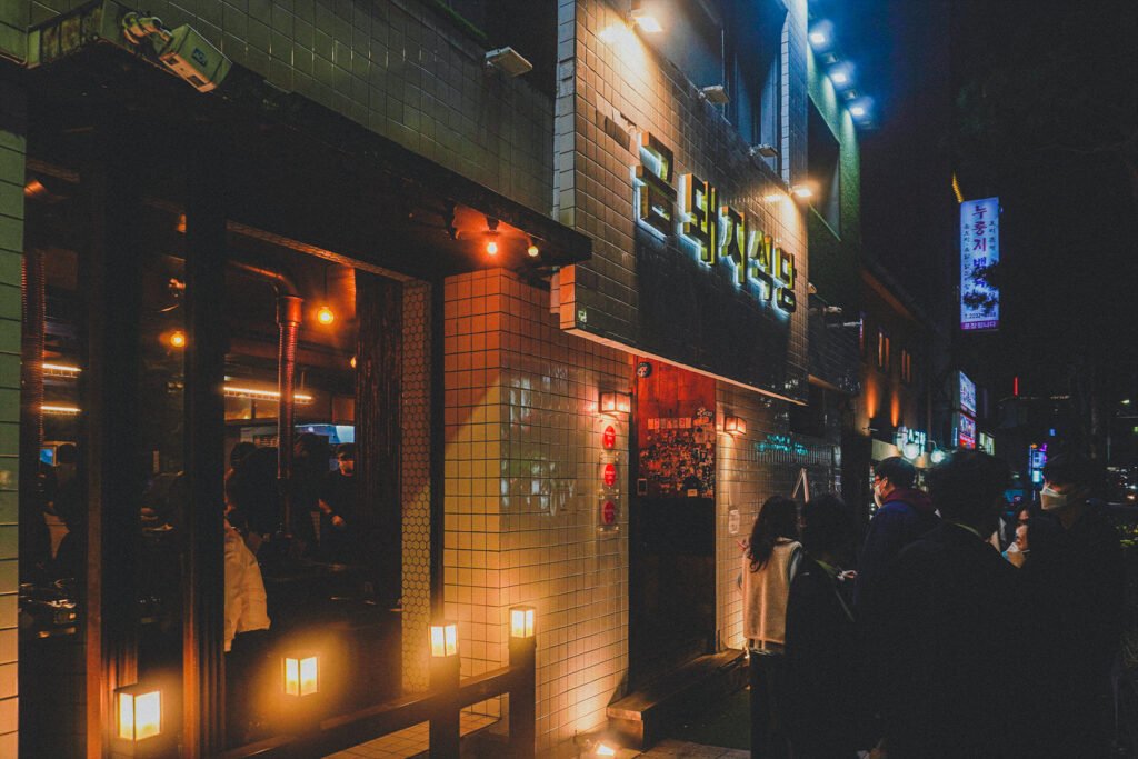 exterior night shot of the restaurant sign with a line of customers waiting outside
