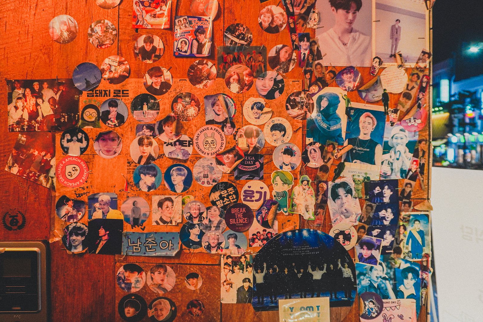 a wall covered in K-pop fan photocards, stickers, and handwritten notes, including a sign reading "금돼지 로드" ("Geumdwaeji Road")
