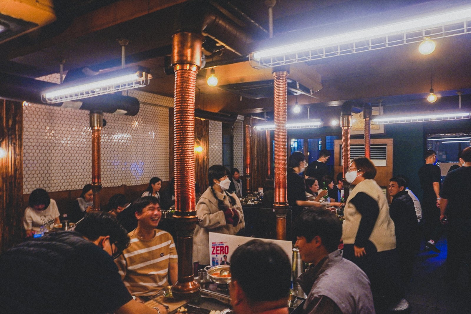 a crowded dining hall with copper exhaust vents hanging over each table