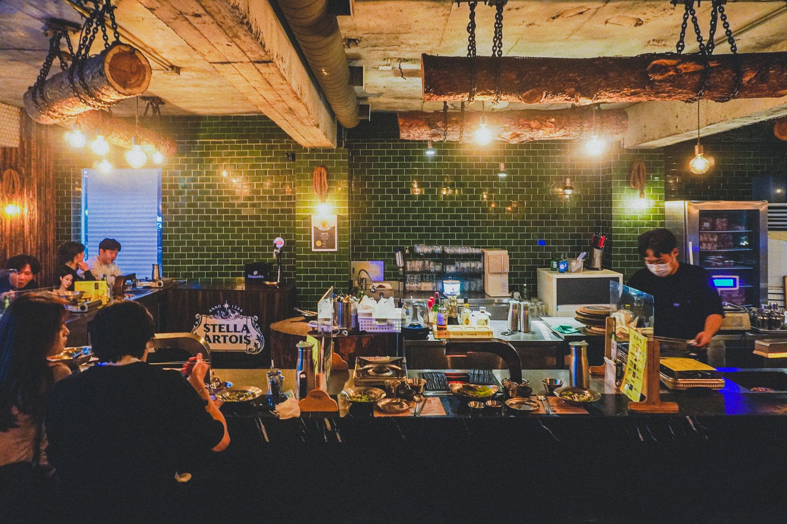a prep counter and bar area with a Stella Artois tap sign, staff working, and glassware lined up