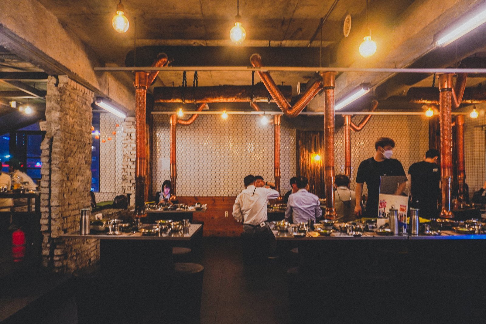 a lower-floor dining area with exposed brick, copper ventilation pipes, and wood-paneled booths