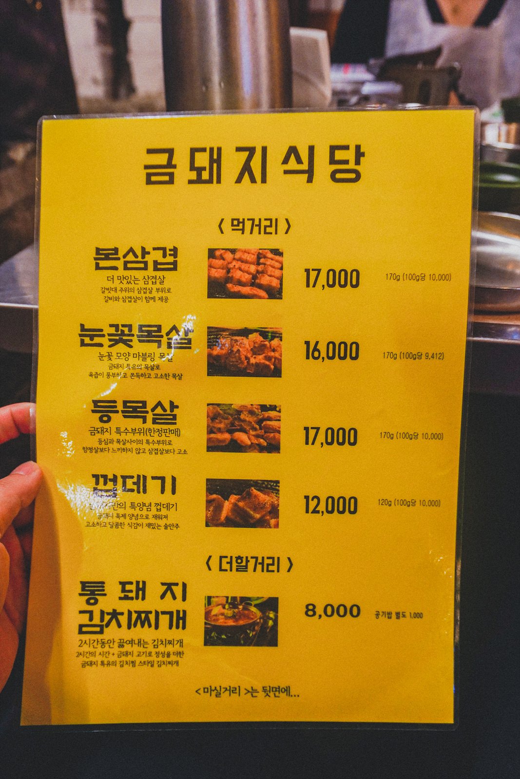 a yellow laminated menu board listing pork cuts, prices, and descriptions in Korean