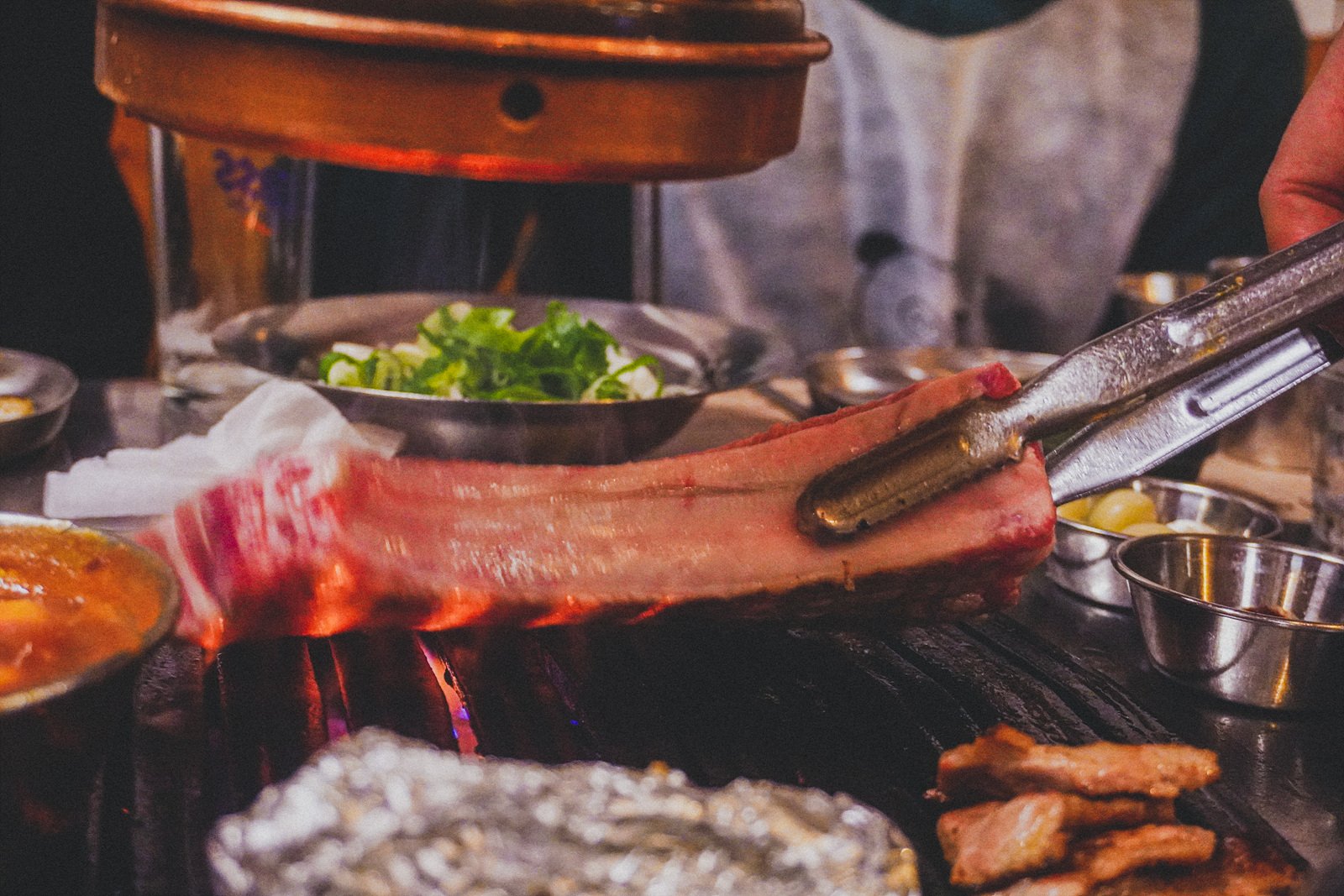 a bone-in rib cut of pork being placed on the grill with tongs