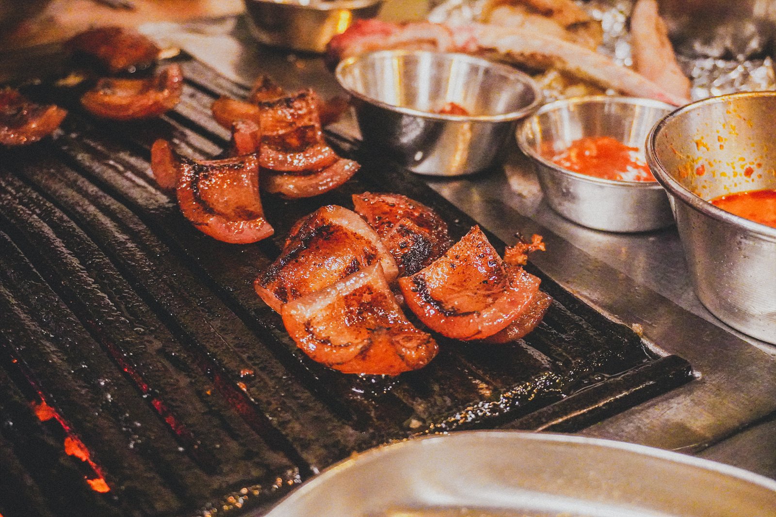 the same pork skin, now grilled golden-brown and sliced into curved pieces, plated near several dipping sauces