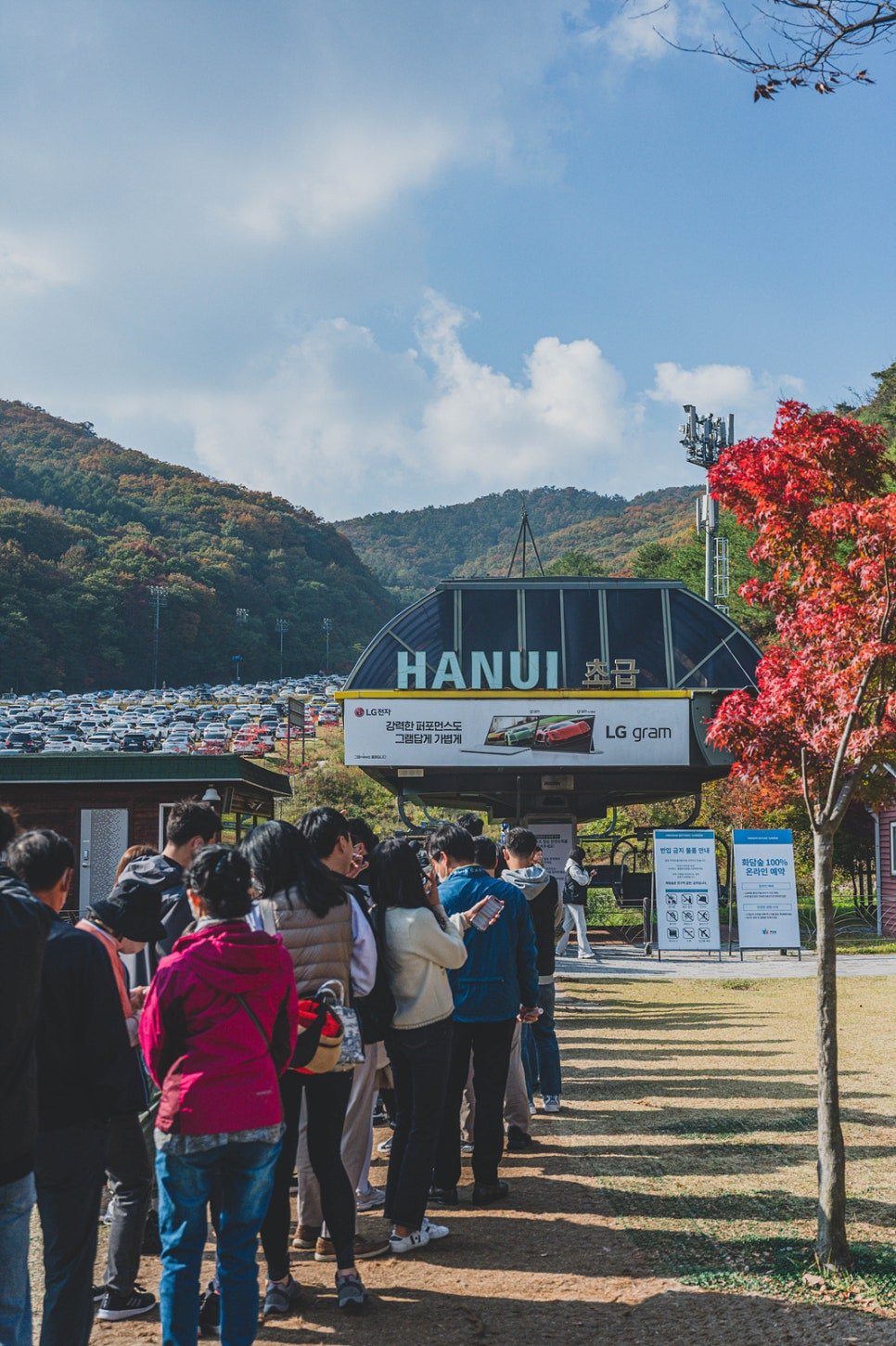 Long queue at the monorail platform, with a full parking lot and autumn color in the background