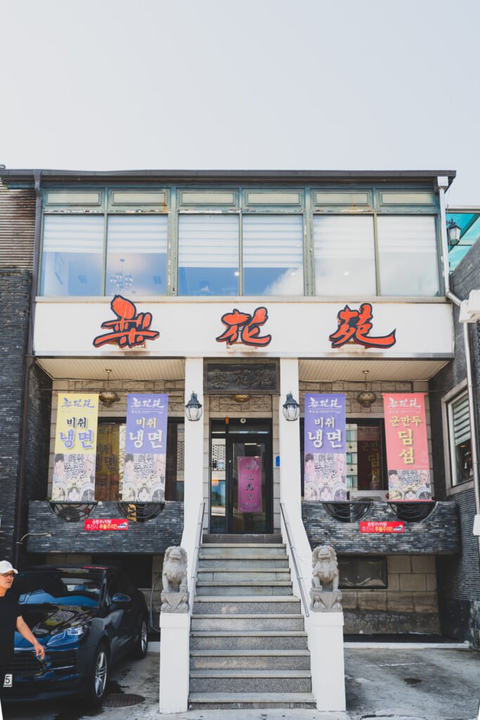 Ihwawon's street-facing facade, red Hanja signage reading 梨花苑 flanked by stone lion statues at the entrance stairs