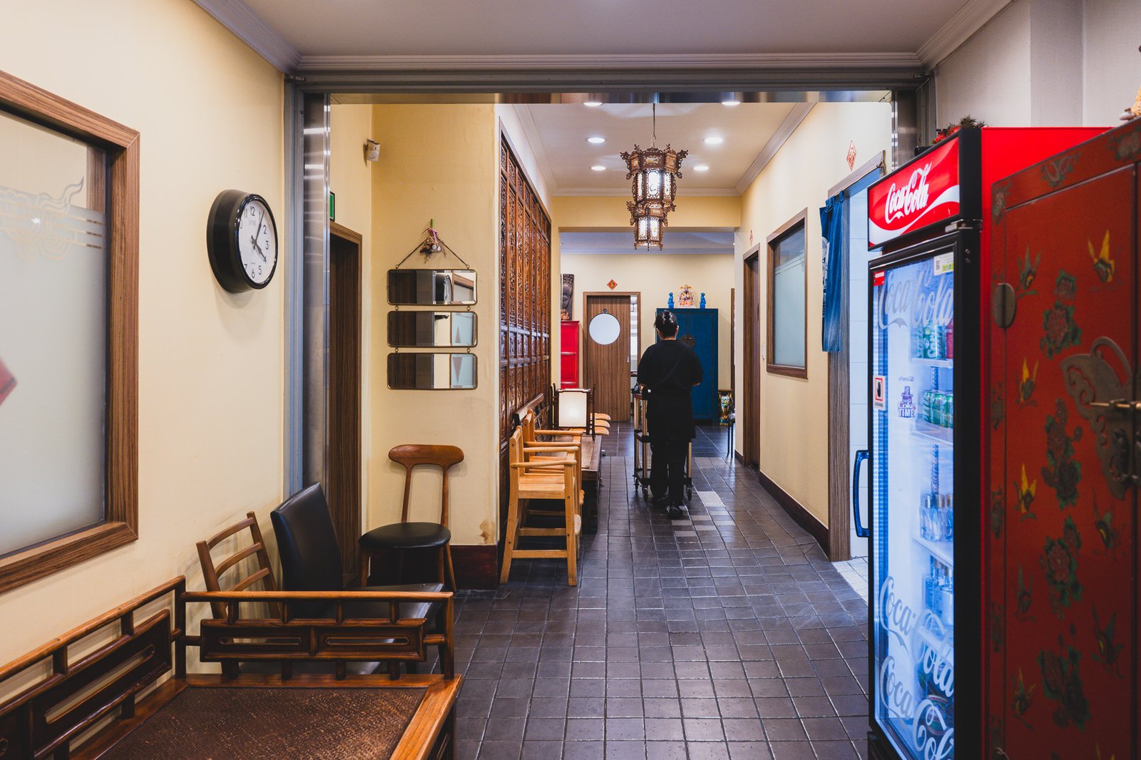Corridor inside Ihwawon lined with carved wooden panels, a hanging lantern, and a staff member pushing a cart toward the dining rooms