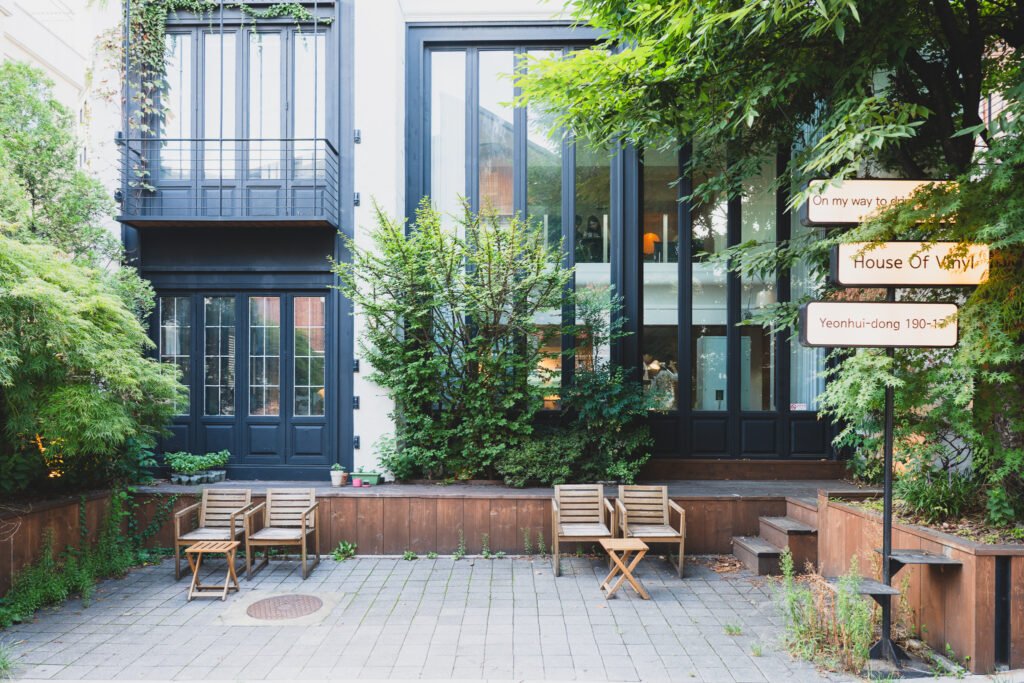 Café exterior at dusk, "House Of Vinyl" signage and outdoor seating under overgrown trees
