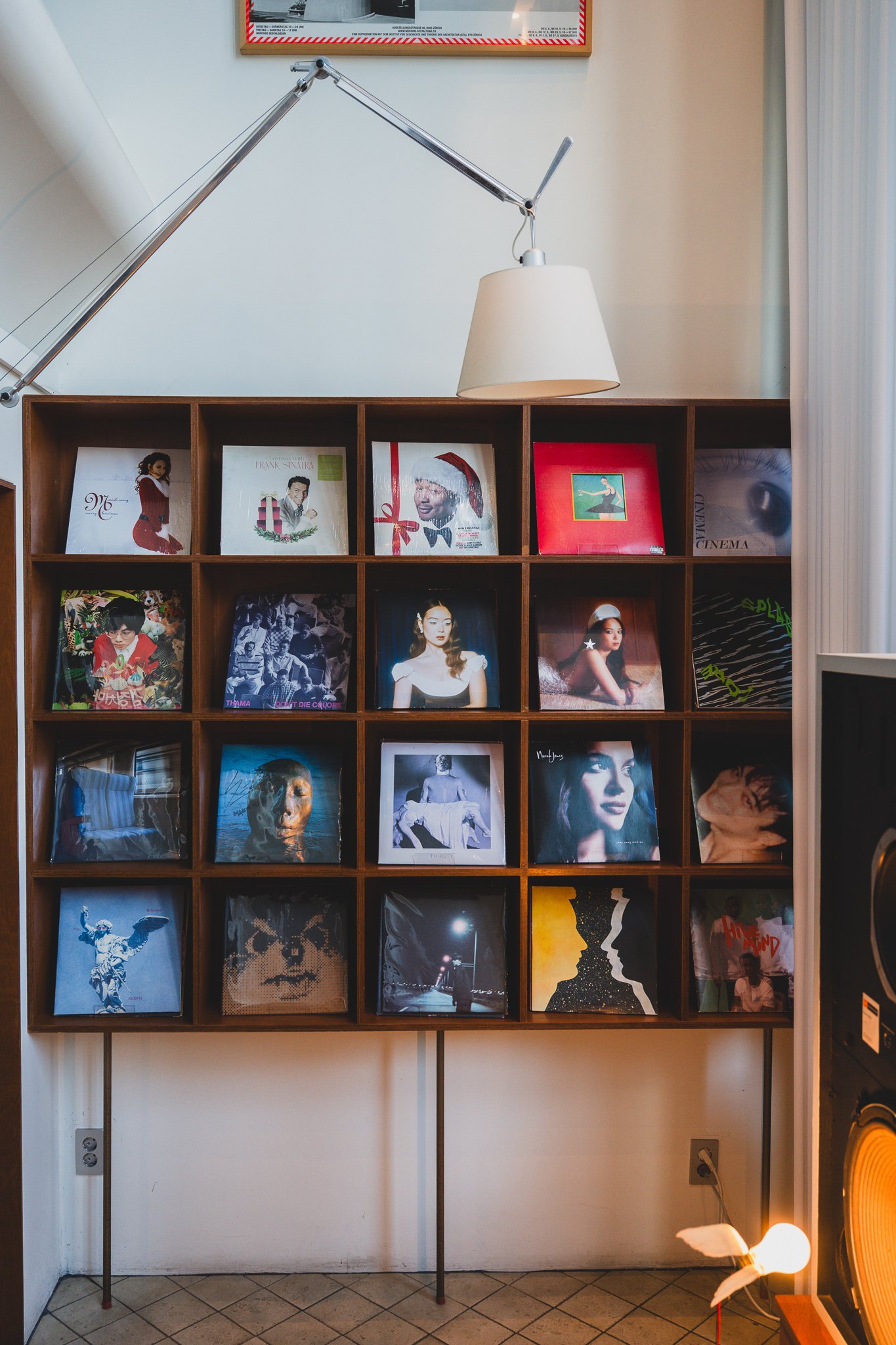 Wall of vinyl records filling built-in wooden shelving, with a Tolomeo lamp nearby
