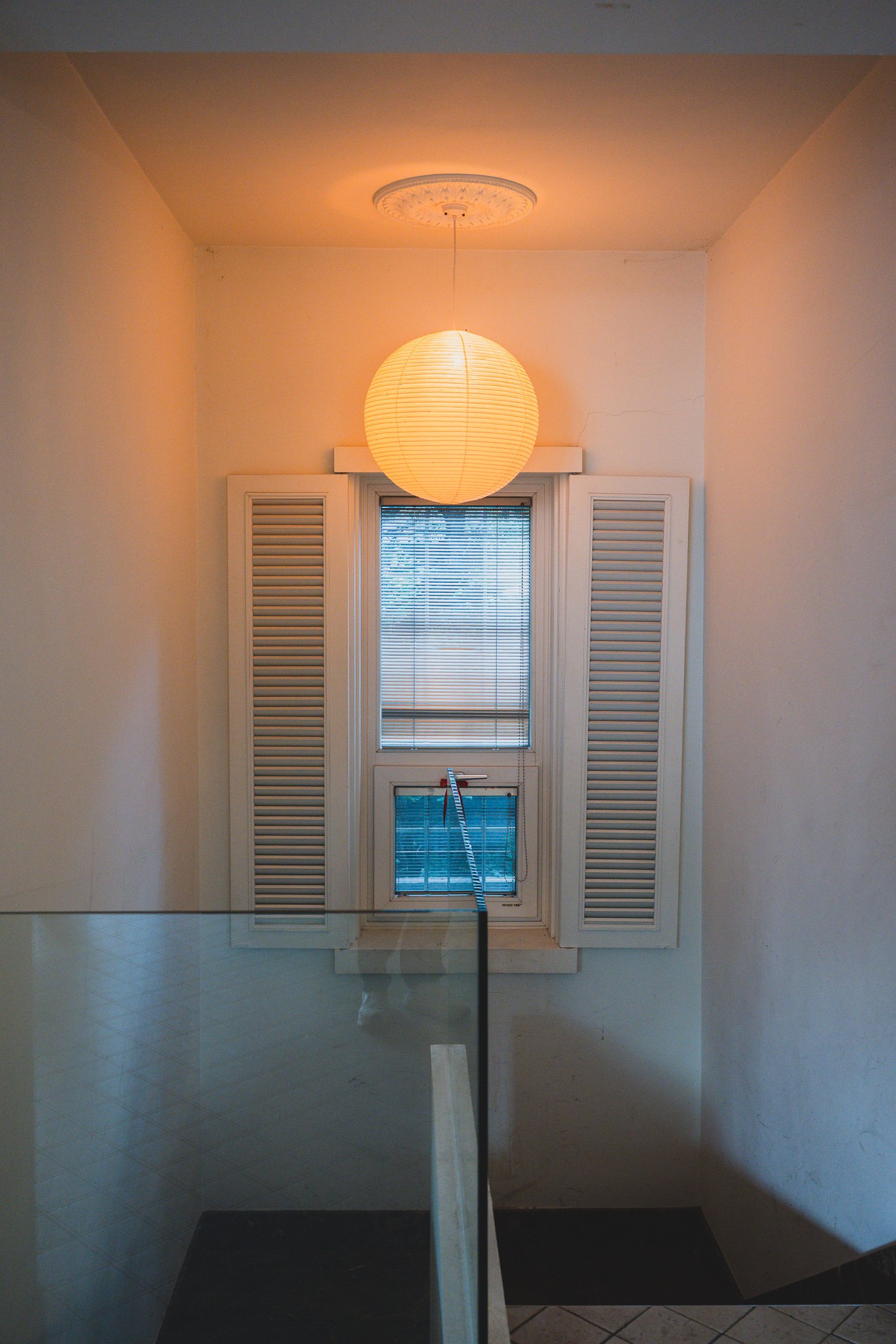 Stairwell landing with a round paper lantern in an Isamu Noguchi style, next to white shuttered windows