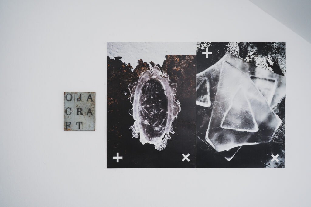 Rusted metal "OJA CRAFT" nameplate mounted on a white wall beside two framed close-up photographs of cast glass texture