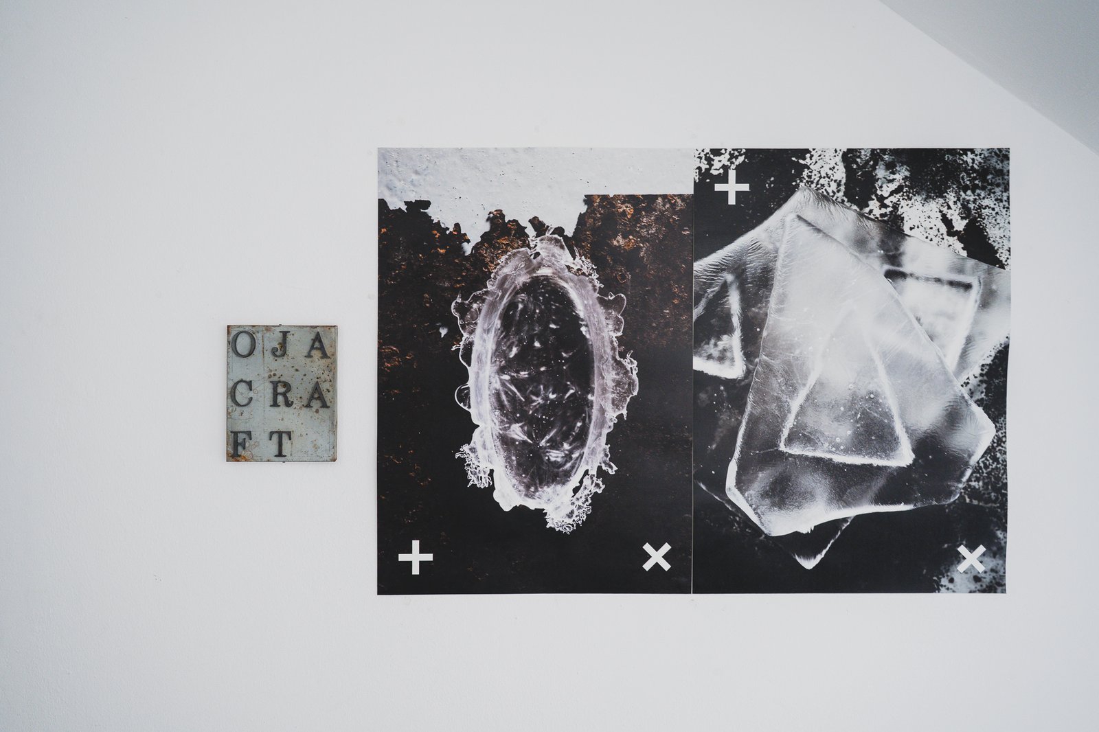 Rusted metal "OJA CRAFT" nameplate mounted on a white wall beside two framed close-up photographs of cast glass texture