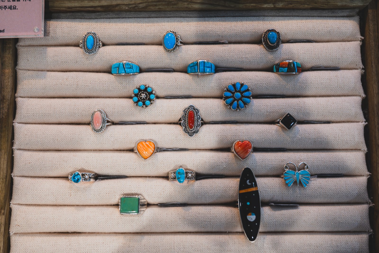 Rows of silver rings set with turquoise, coral, black onyx, and a night-sky patterned inlay, laid flat on a canvas display tray
