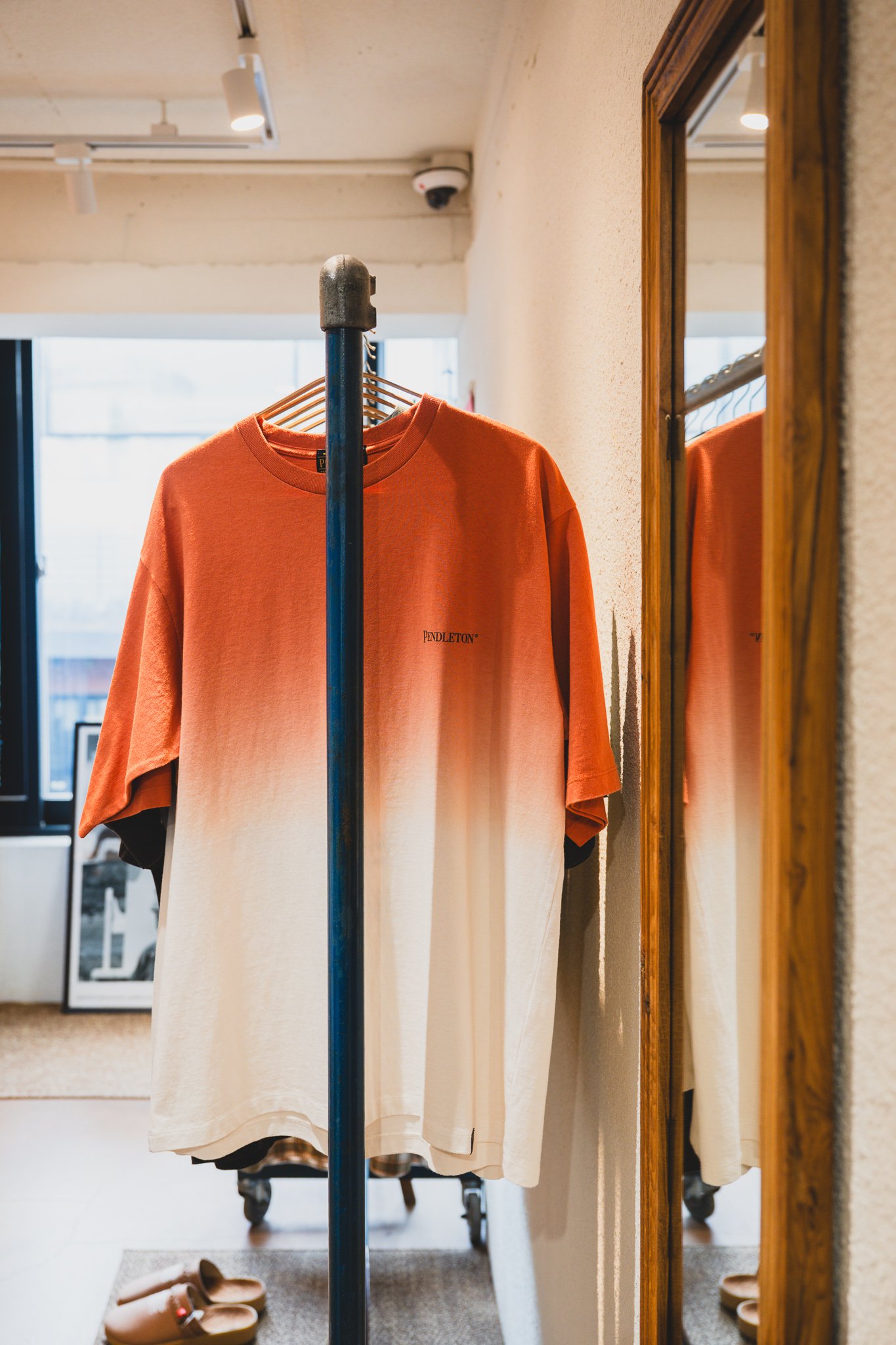 Orange-to-cream ombre-dyed Pendleton T-shirt on a clothing rack, reflected in a full-length mirror nearby