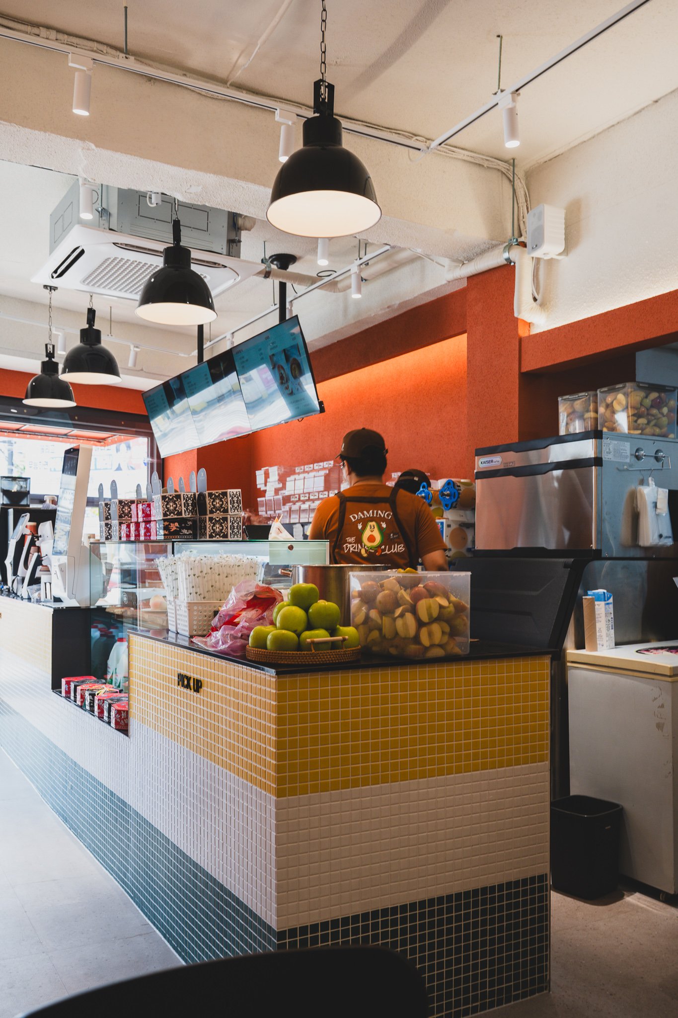 Counter and pickup area with staff wearing "DAMING THE DRINK CLUB" aprons featuring an avocado logo
