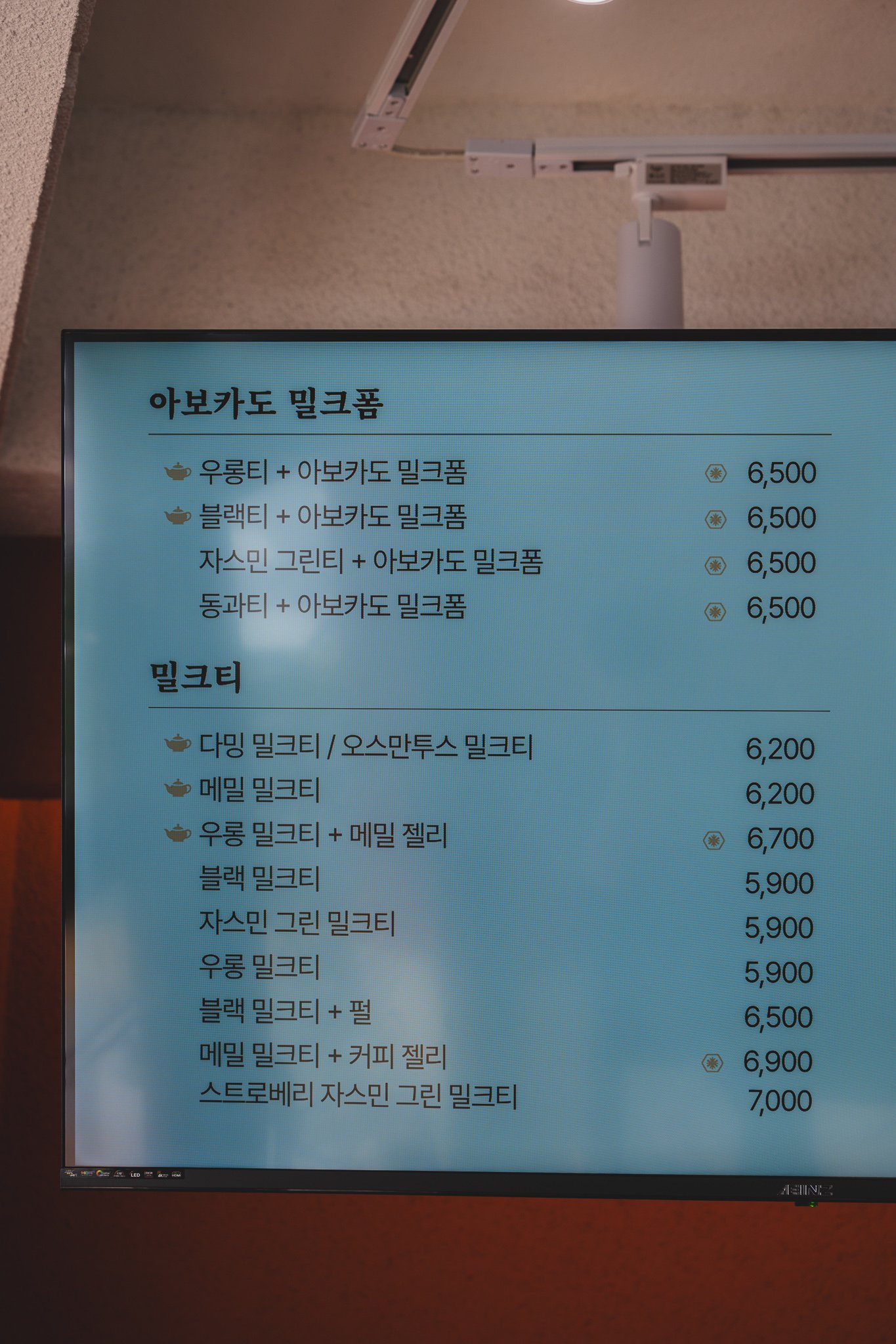 Wall-mounted screen menu showing four Avocado Milk Foam drinks (each 6,500 KRW) and the milk tea lineup