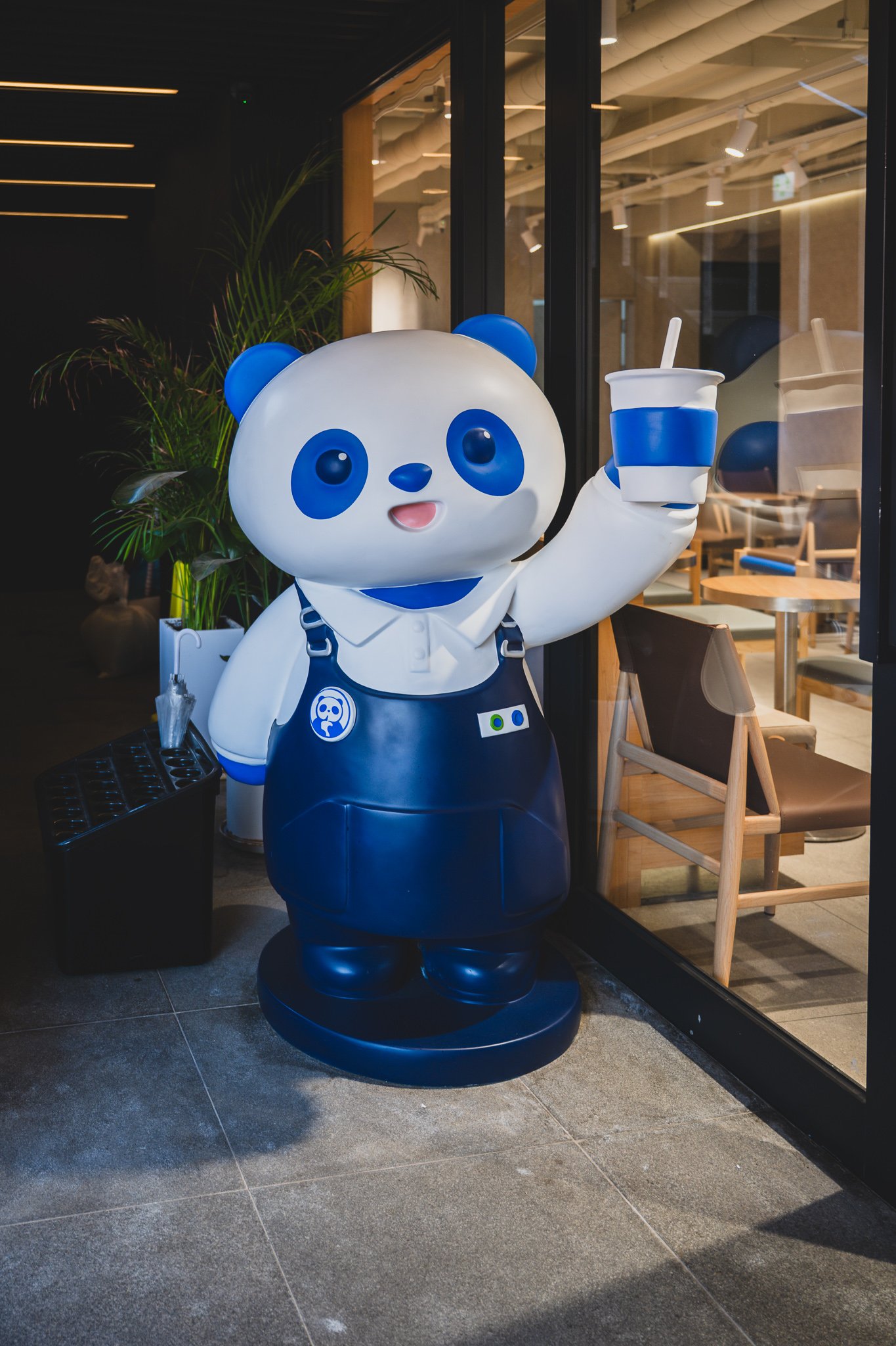 Life-size panda mascot statue at the entrance, holding a drink cup and waving