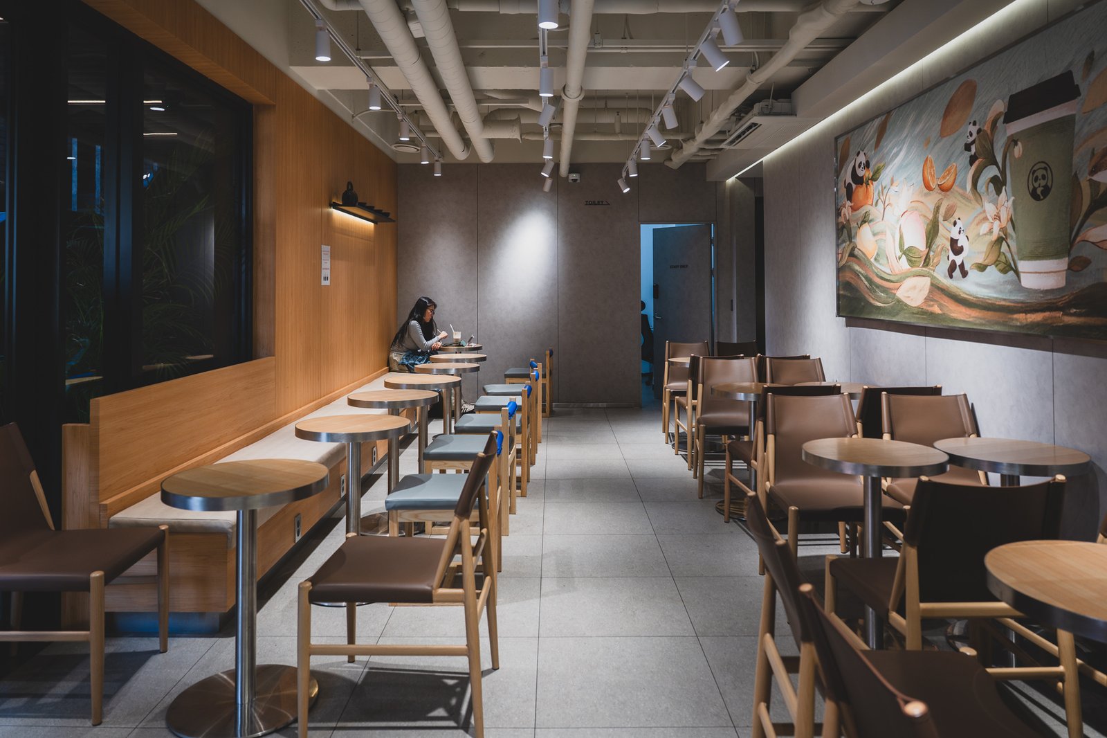 Interior seating with wood-tone benches and leather chairs, panda illustration on the wall