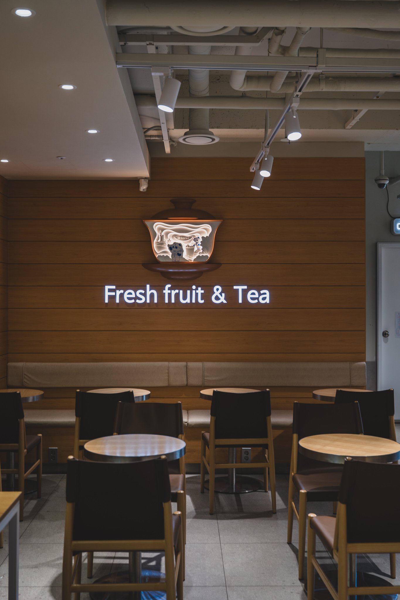 Illuminated "Fresh fruit & Tea" sign on the wall above a row of seating