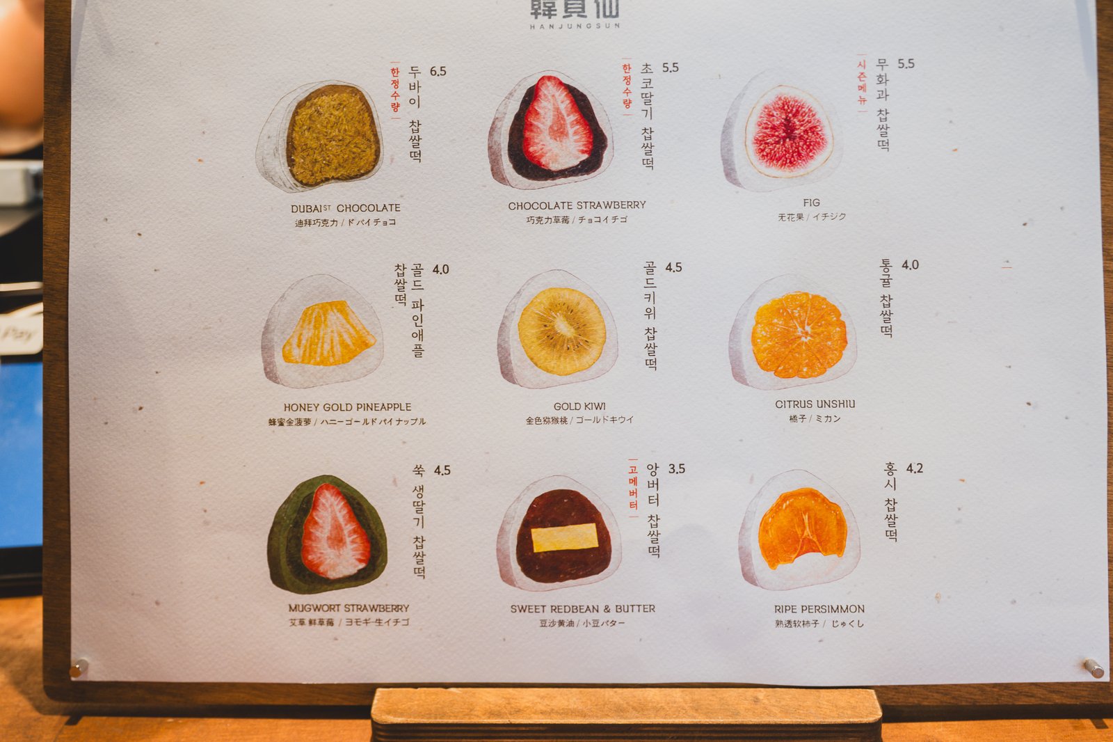 Full menu board showing nine mochi flavors with prices, including Dubai-style Chocolate, Chocolate Strawberry, and Fig