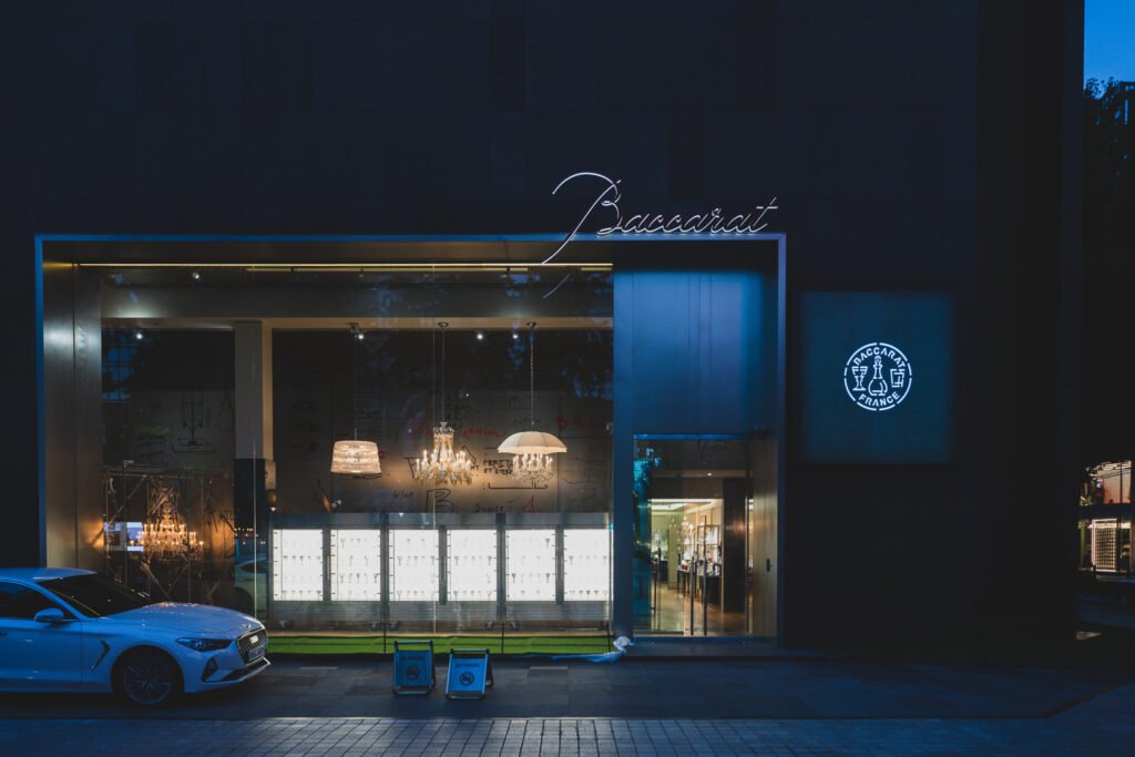 The exterior of Maison Baccarat Seoul on Dosan-daero at night, chandelier light glowing through the storefront glass