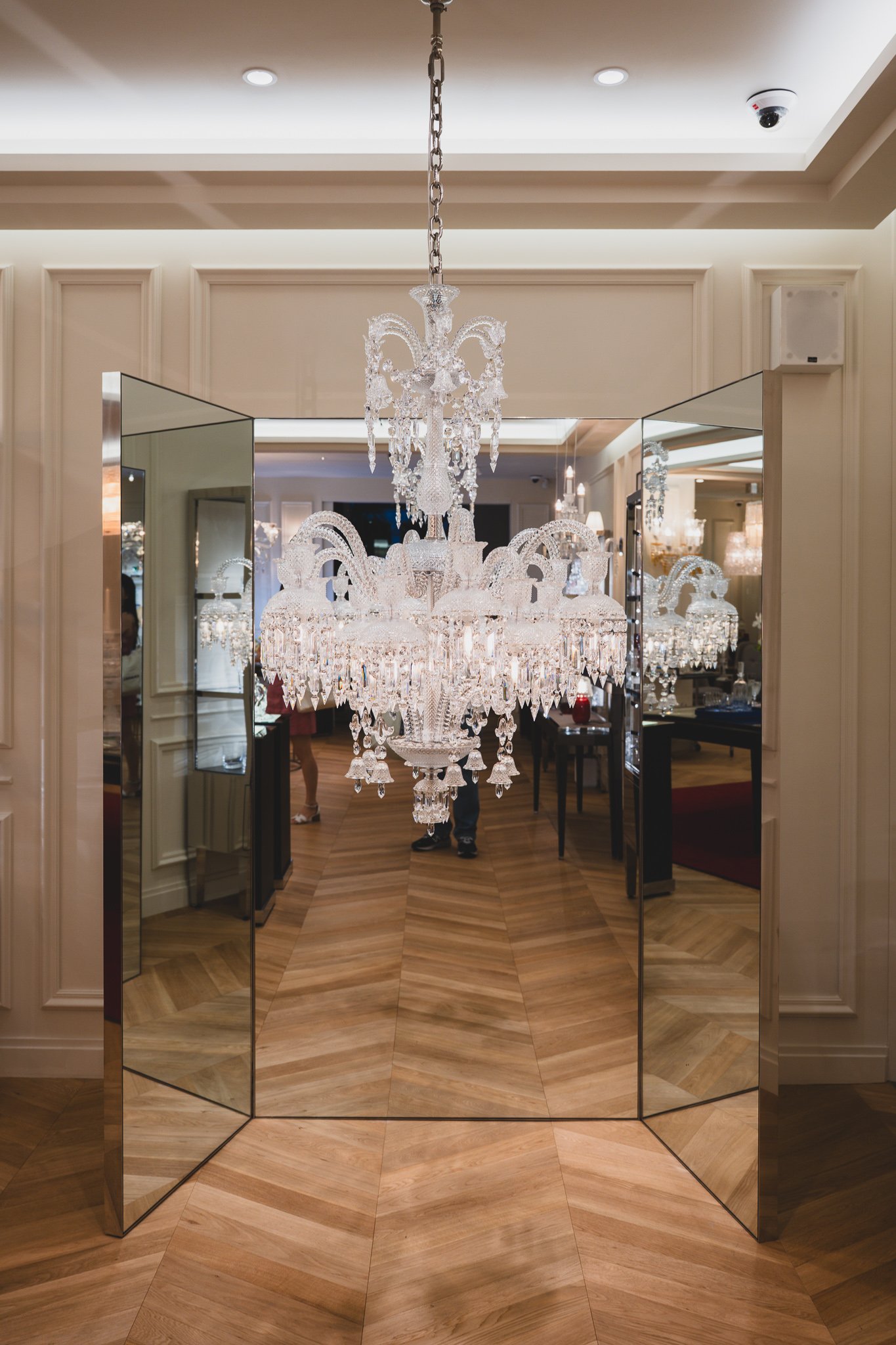 A large chandelier hanging in a mirrored corridor at the center of the showroom, its reflection repeating into apparent infinity