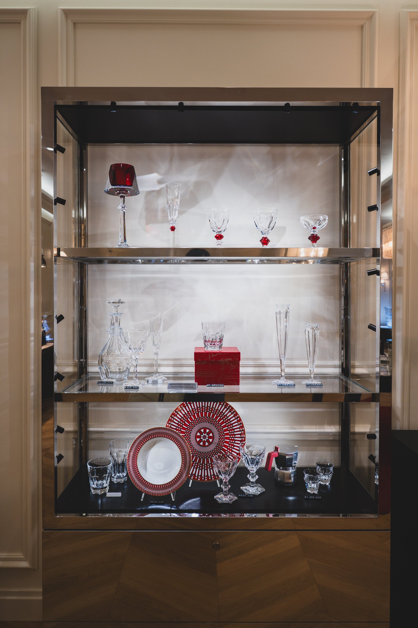 A glass cabinet displaying red, blue, and green crystal tumblers and decanters