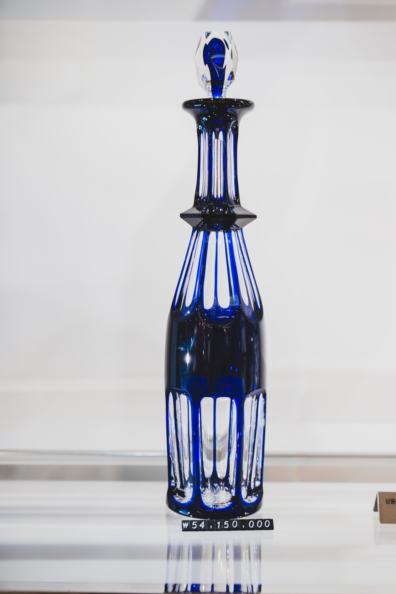 A cobalt-blue crystal decanter lit under a spotlight in a display cabinet