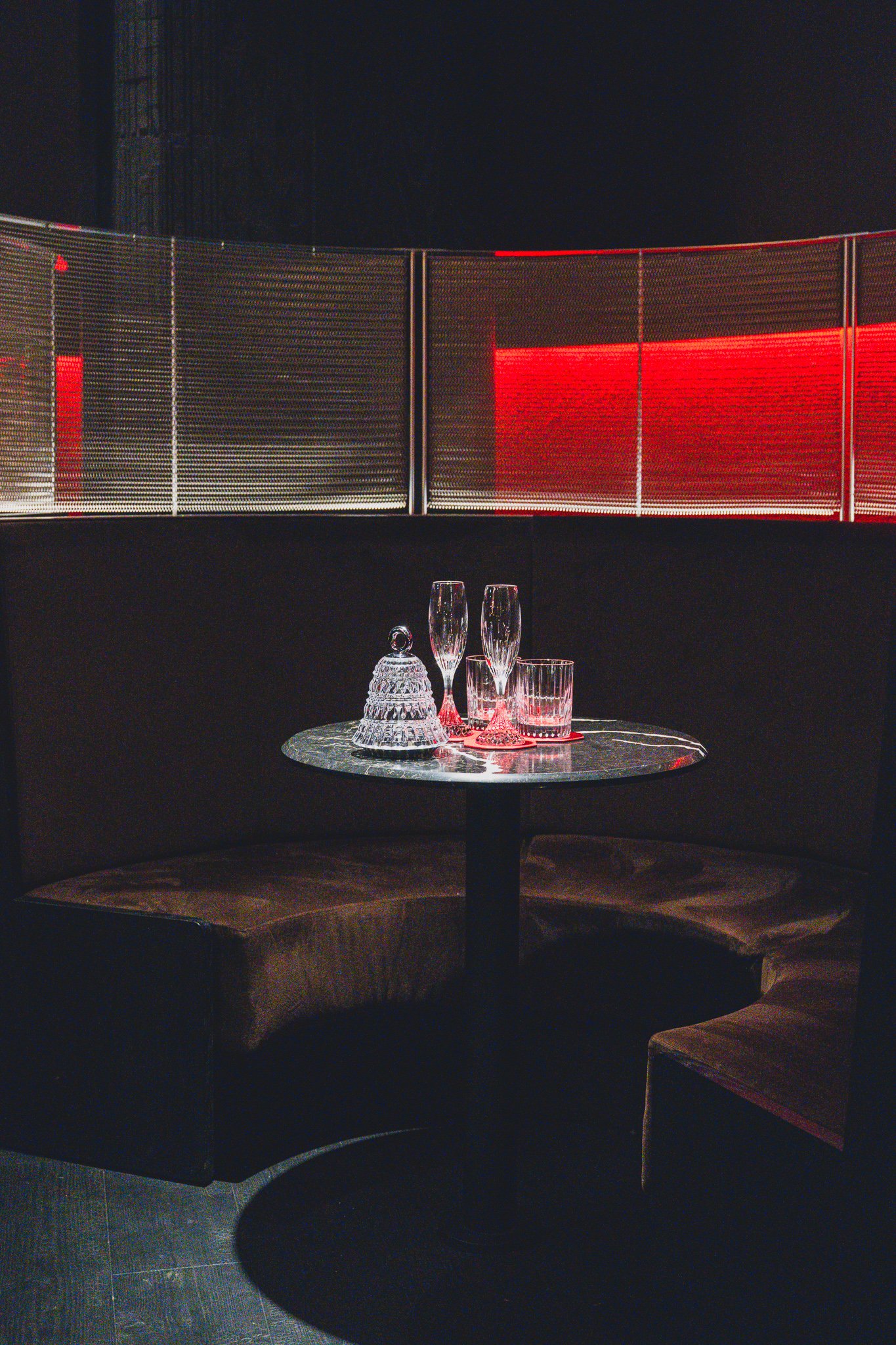A semicircular sofa and round tables making up the hall seating area, lit in red