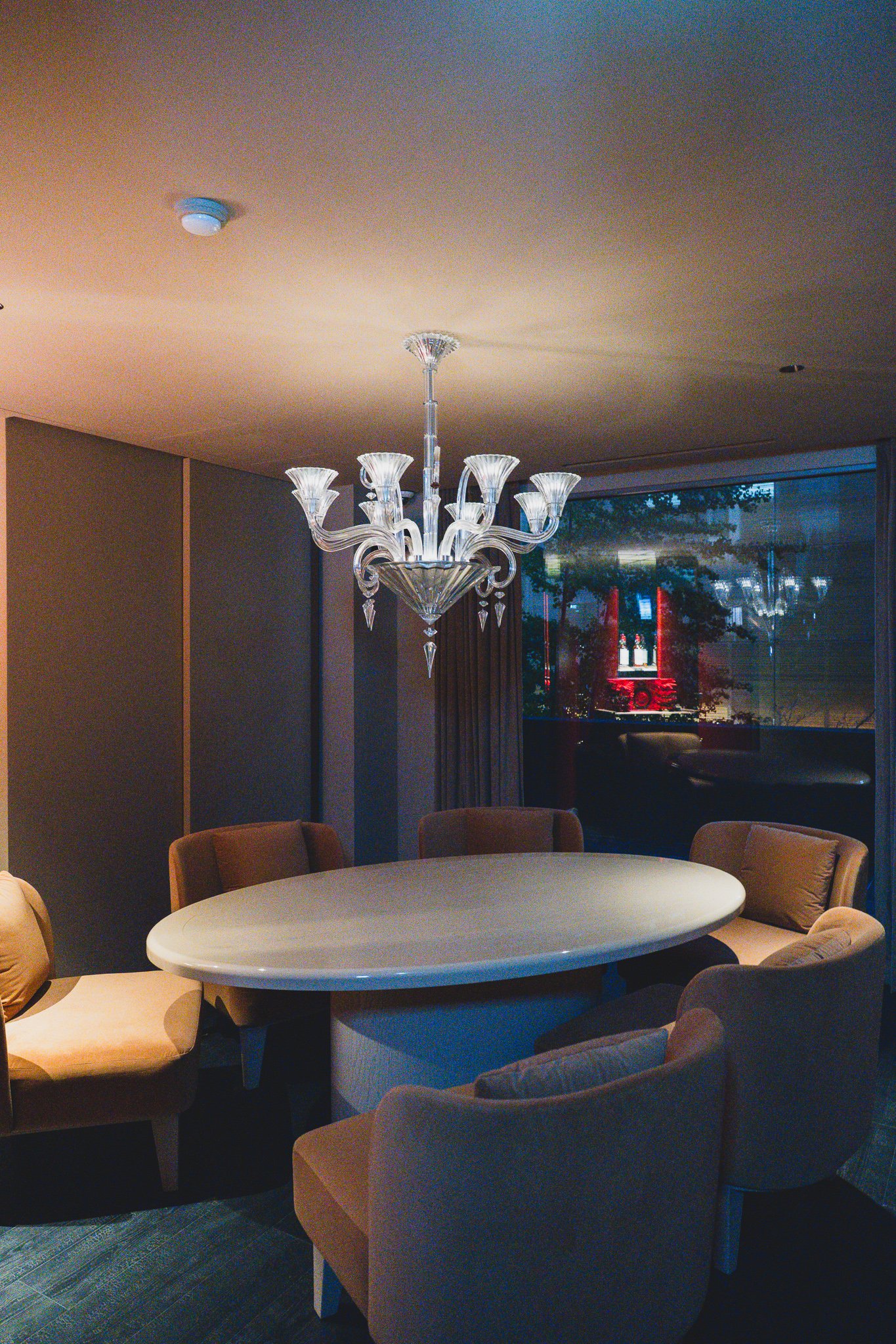 A bright private room with a white oval dining table, brown leather armchairs, and a low-hung crystal chandelier