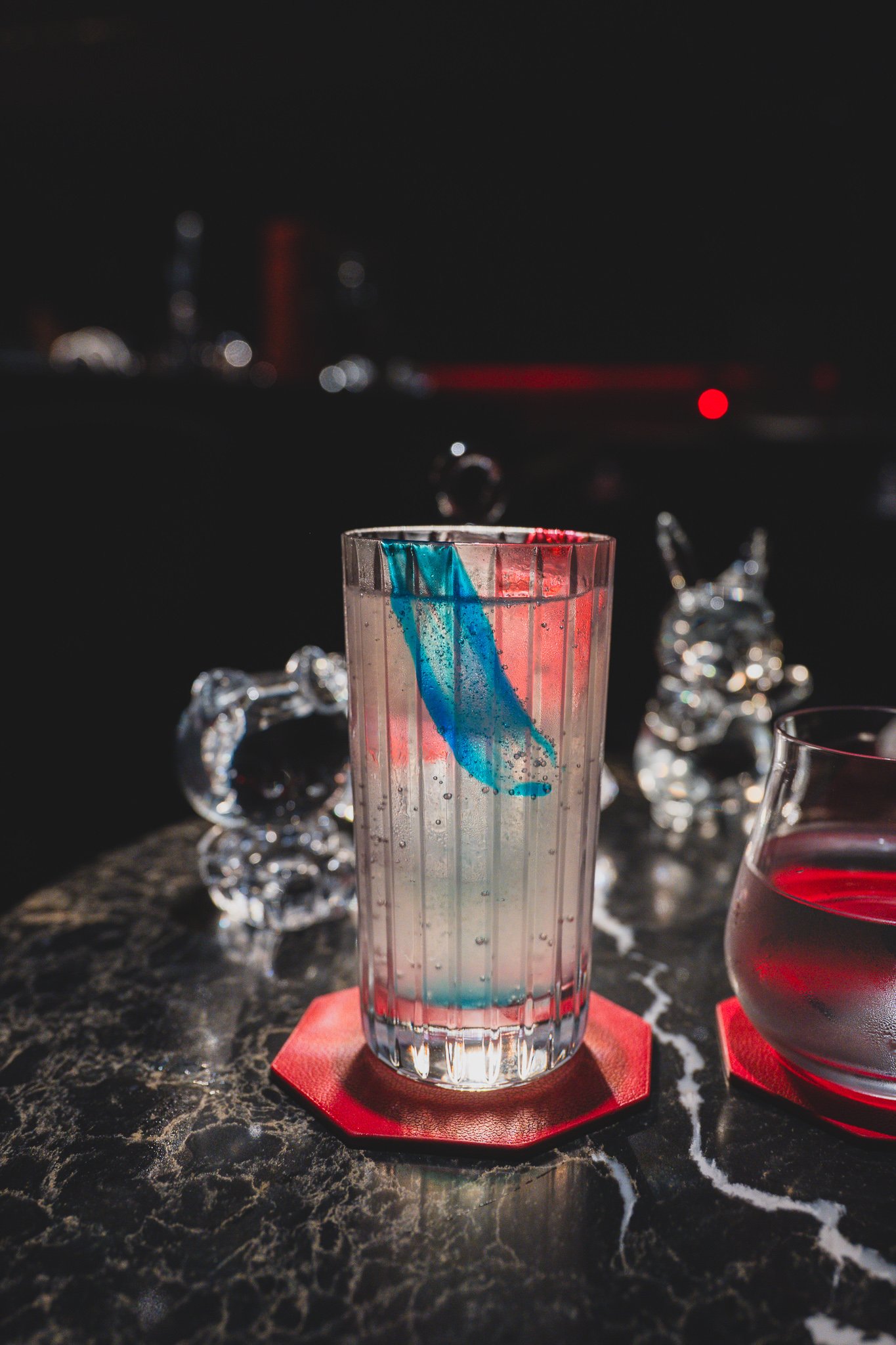 A highball glass of the Lost & New cocktail, blue and pink streaks running through clear tonic water