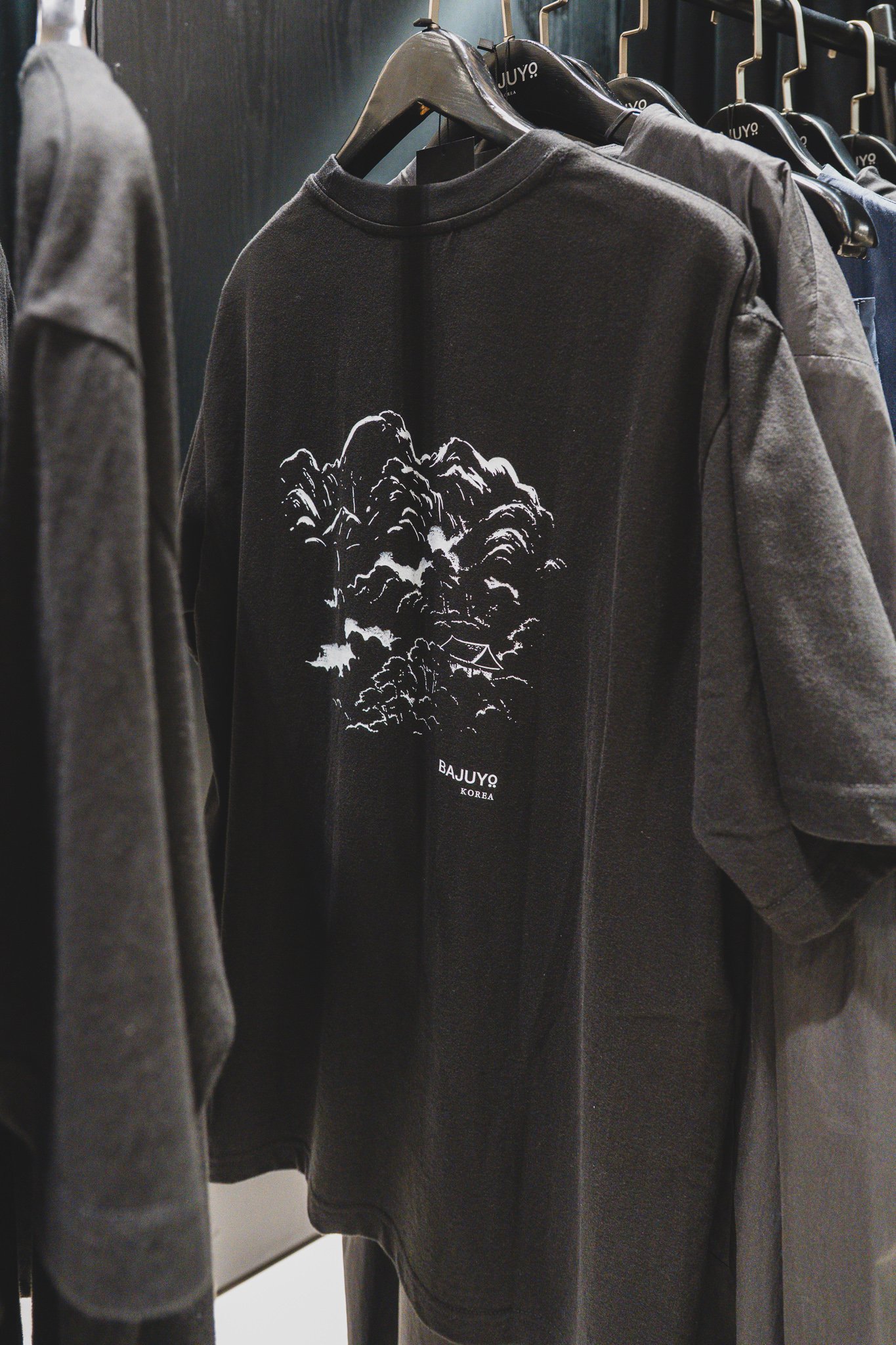 BAJUYO t-shirt with an ink-wash-style landscape print on the back, hiding a hanok roofline among the hills