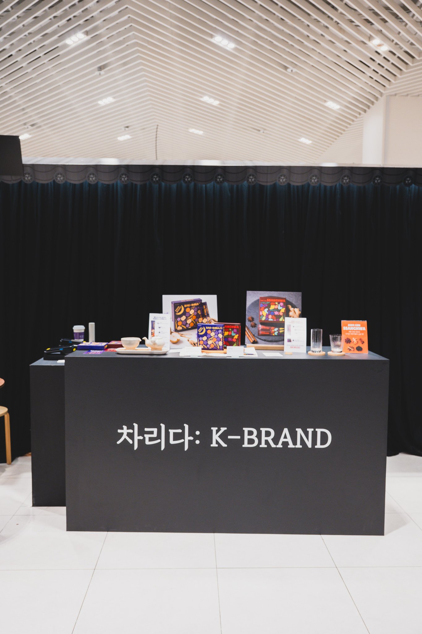 K-BRAND corner display with snack and tea-stick packaging on a black counter