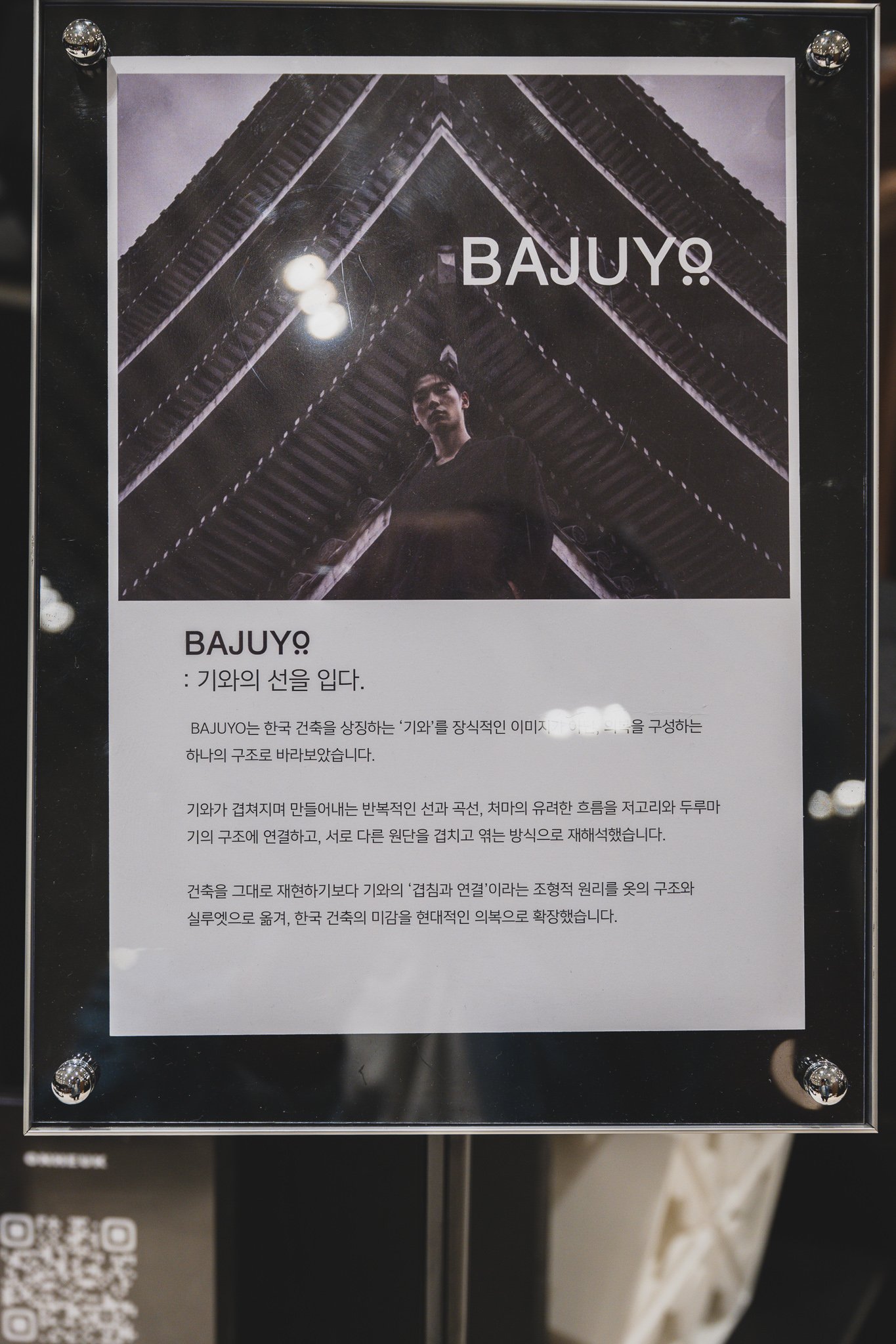 BAJUYO brand panel reading "Wearing the Line of the Roof Tile," with a figure standing beneath a hanok eave