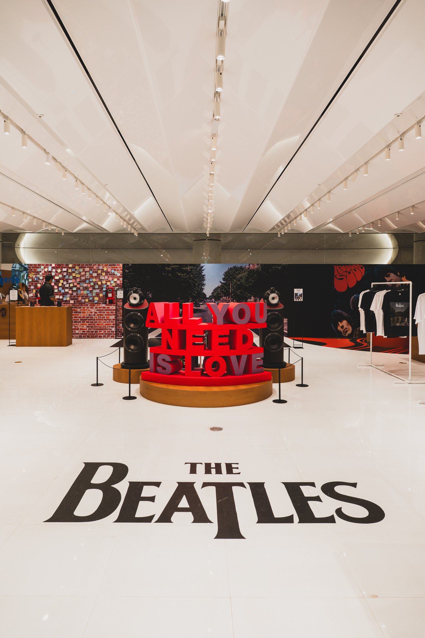 Red "ALL YOU NEED IS LOVE" sculpture between two speakers, with Abbey Road photography and Rubber Soul album art in the background