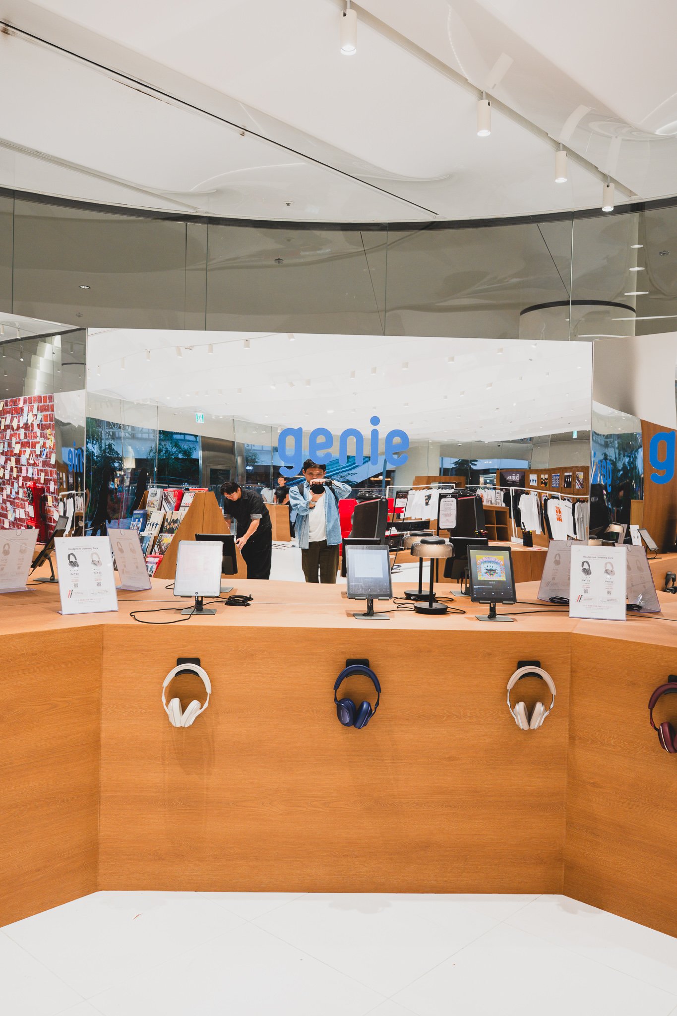 Listening zone with multiple headphones mounted on a wall next to a Genie Music logo and tablet stands