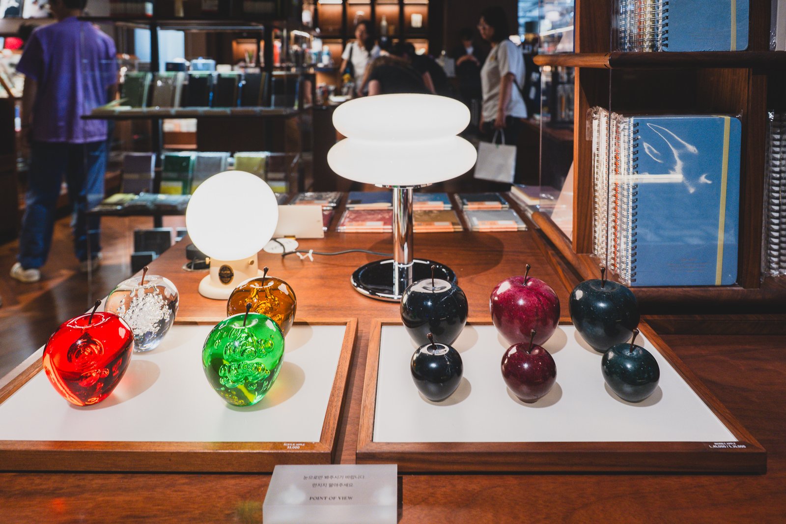 Glass display case with an apple-shaped object and lighting, notebook shelving visible in the background