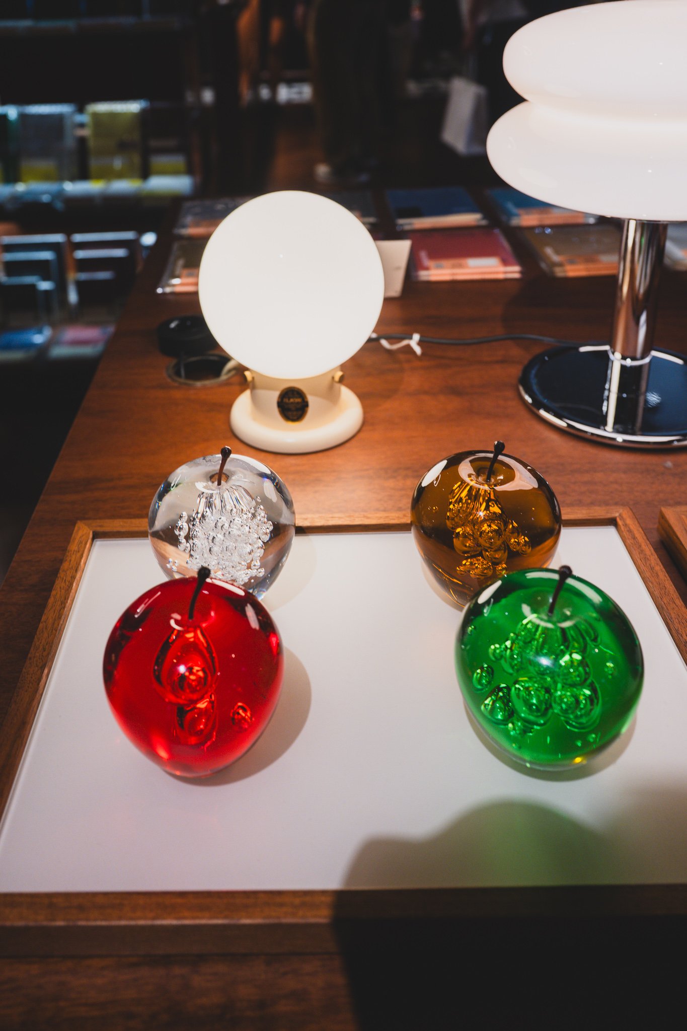 Red, green, amber, and clear glass apple paperweights next to black, burgundy, and dark green marble apple objects