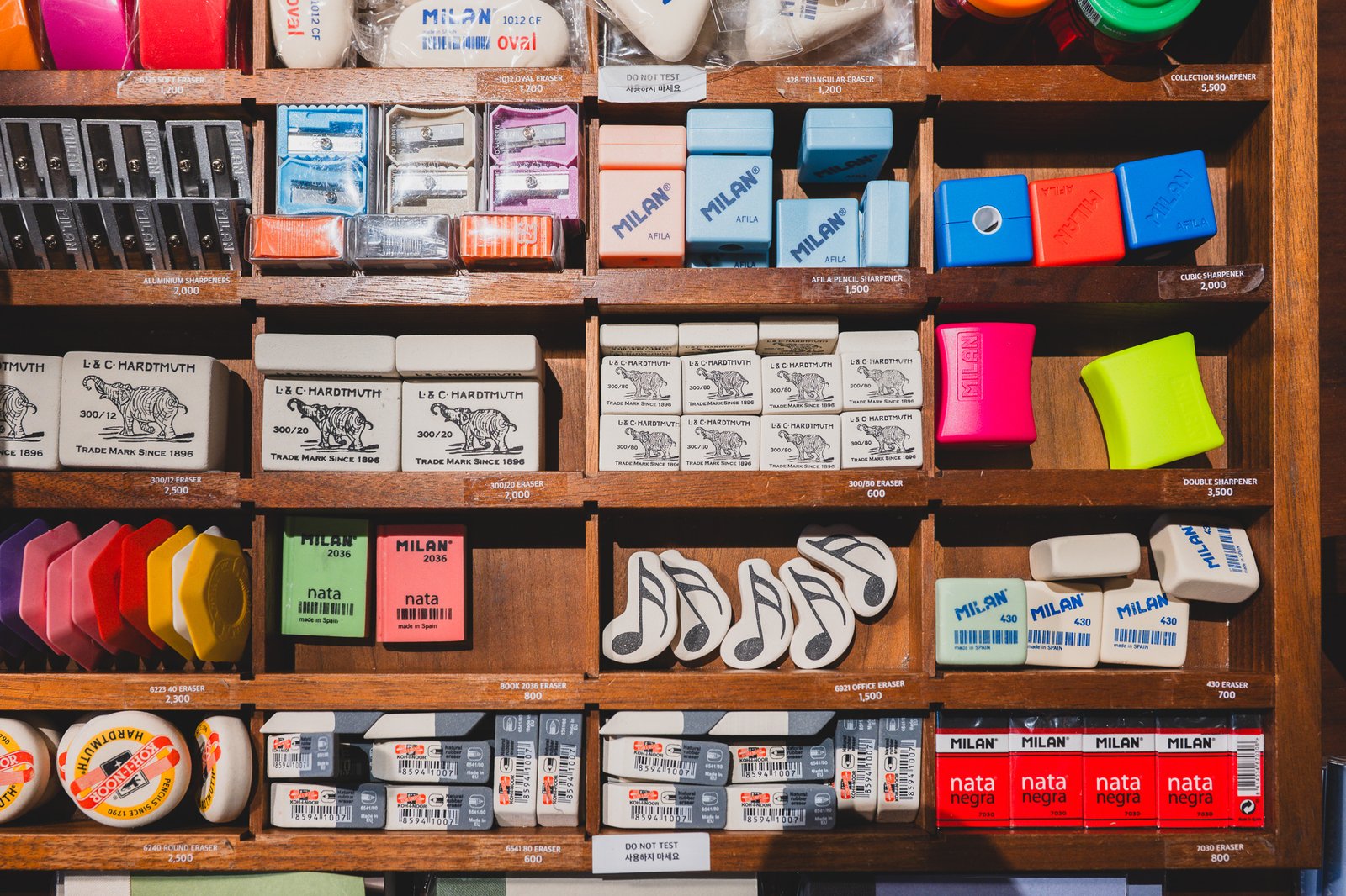 Wall of erasers and sharpeners from brands like Milan and Koh-i-noor Hardtmuth, organized in labeled compartments