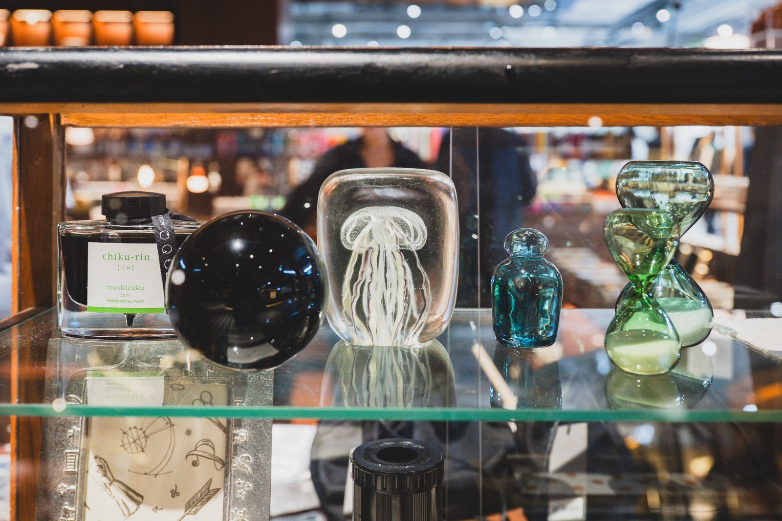 Iroshizuku ink bottle next to a black orb object, a glass piece with a sealed jellyfish, a teal glass bottle, and a green hourglass