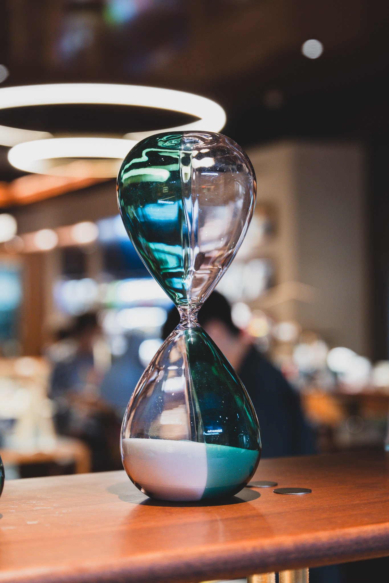 Close-up of a green-and-clear glass hourglass under lighting