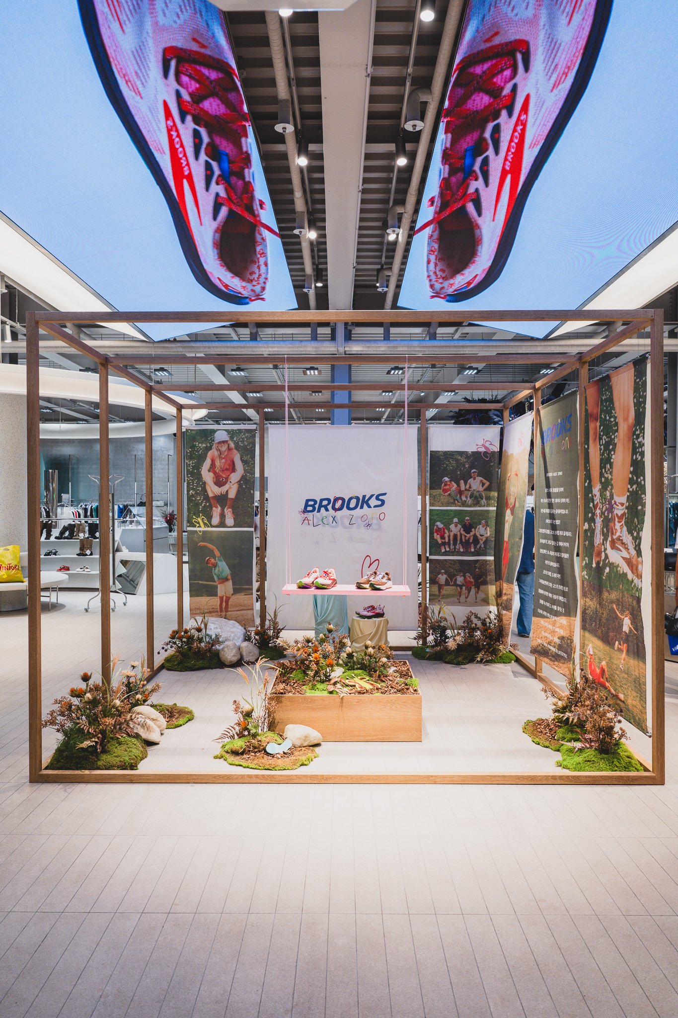Wooden-framed installation booth with an oversized shoe-sole graphic overhead and moss and dried flowers covering the floor