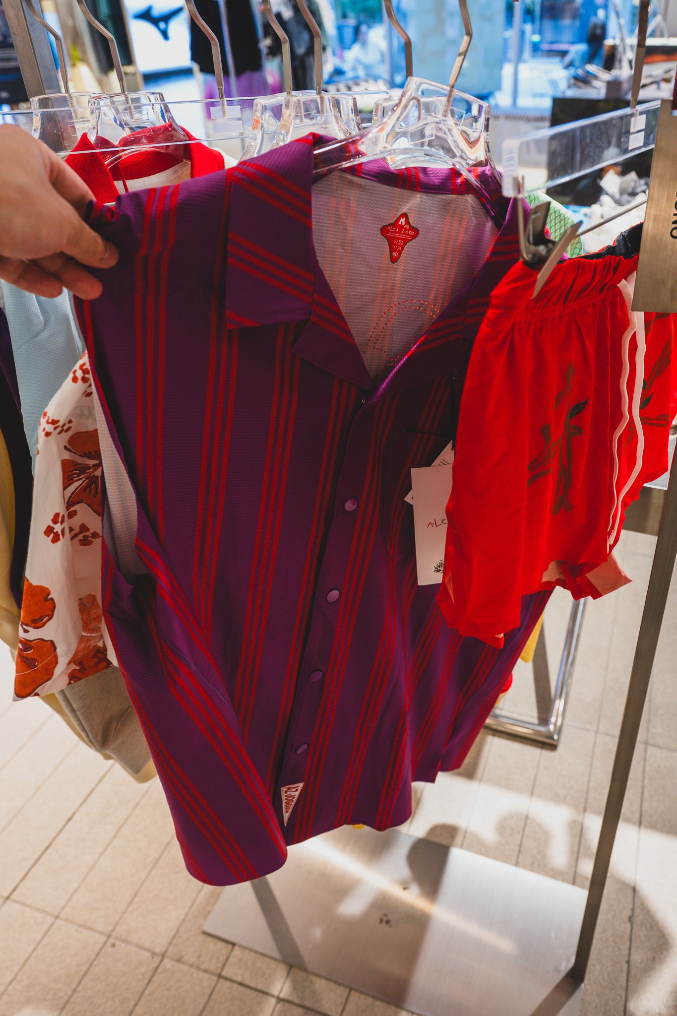 Person holding up a purple-and-red striped polo shirt next to red shorts