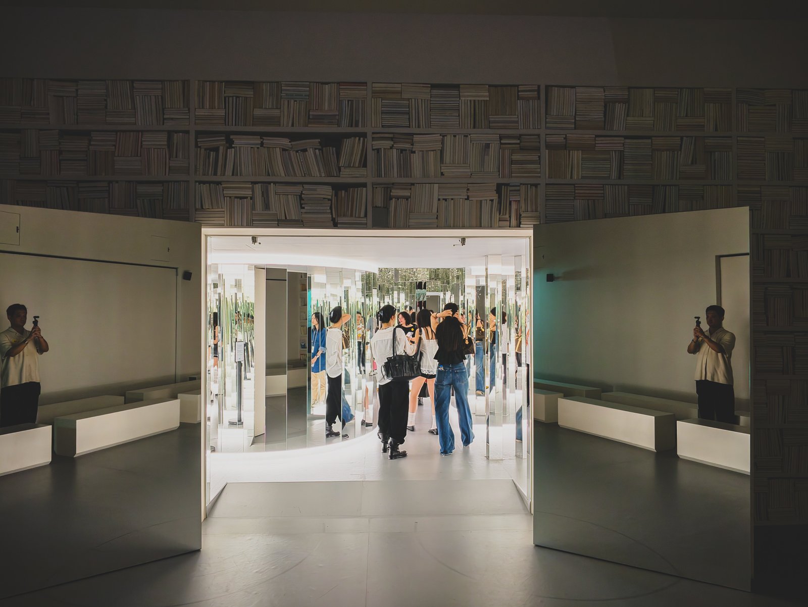 The wall of bookshelves splitting open to reveal the mirror maze entrance, visitors moving inside