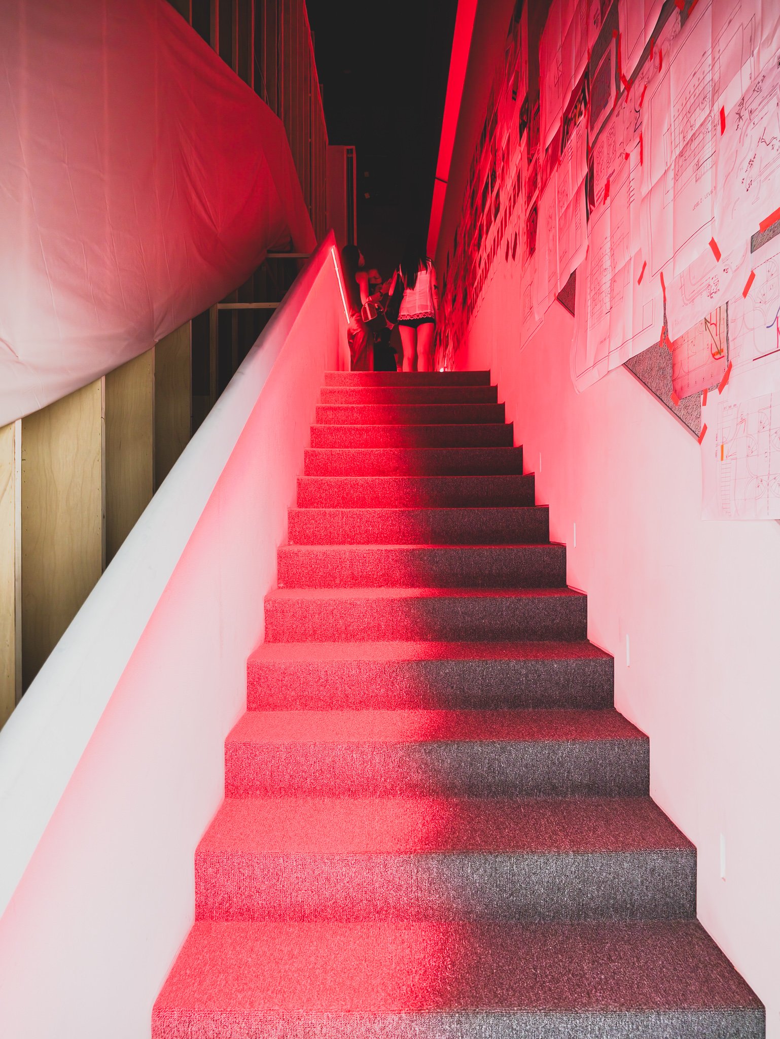 Red-lit staircase covered wall-to-wall with the mirror maze's original architectural drawings and archive sketches