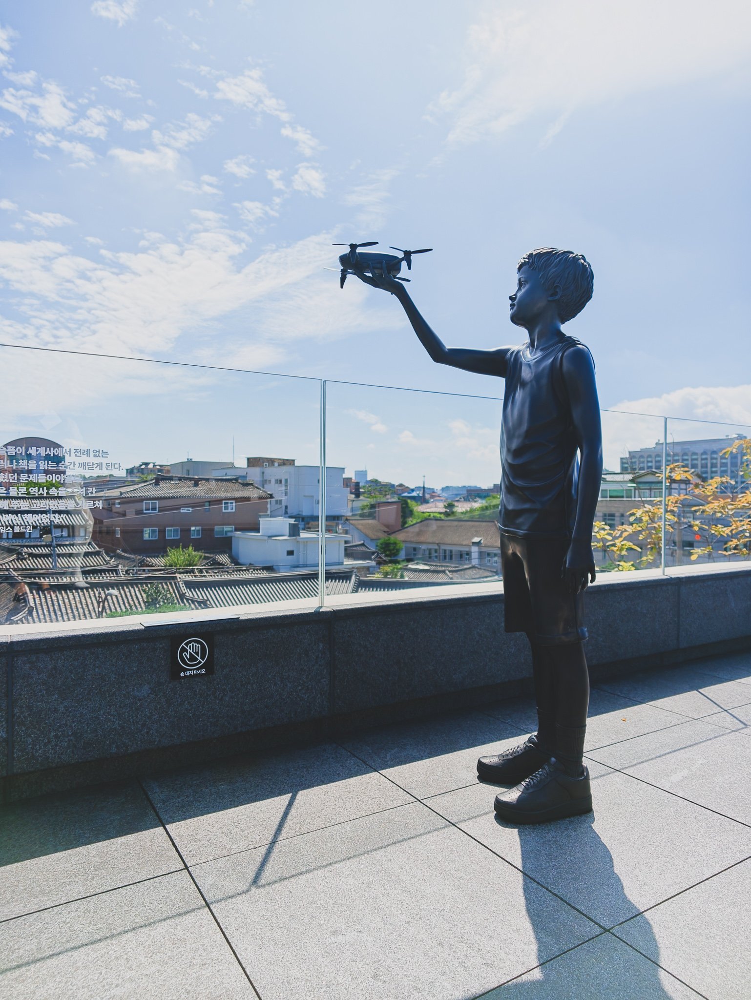 Sculpture of a boy holding a drone, overlooking the Seoul skyline