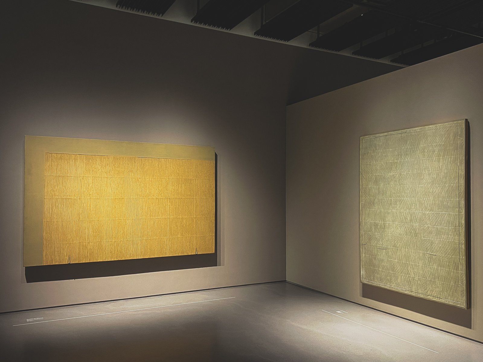 Two works sharing a wall in Space 2 — Park's yellow hanji Ecriture beside one of Dodinh's mineral-pigment paintings, its faint grid emerging from dozens of layered coats