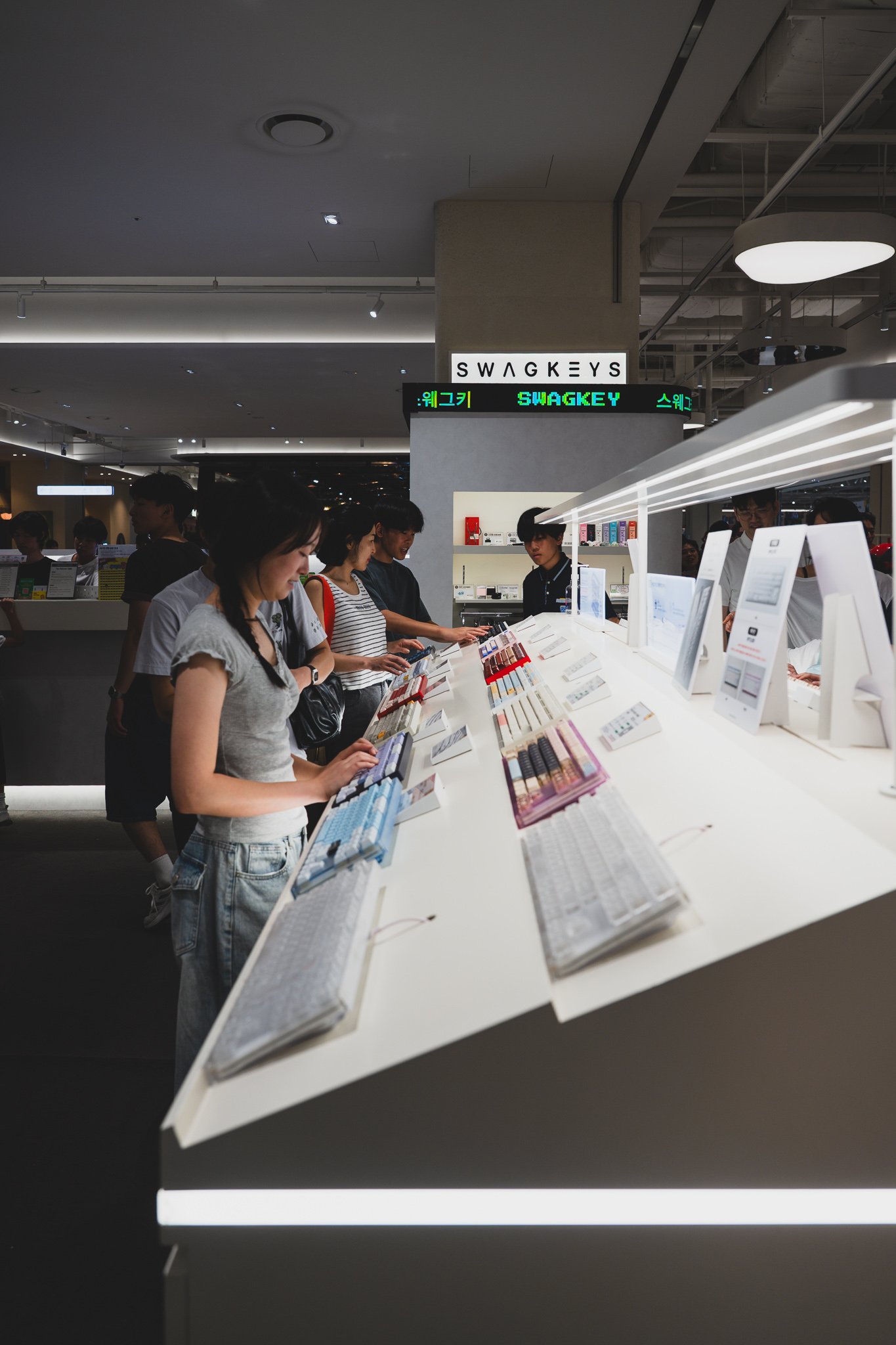 Rows of mechanical keyboards laid out along a long counter, with several people testing different models at once